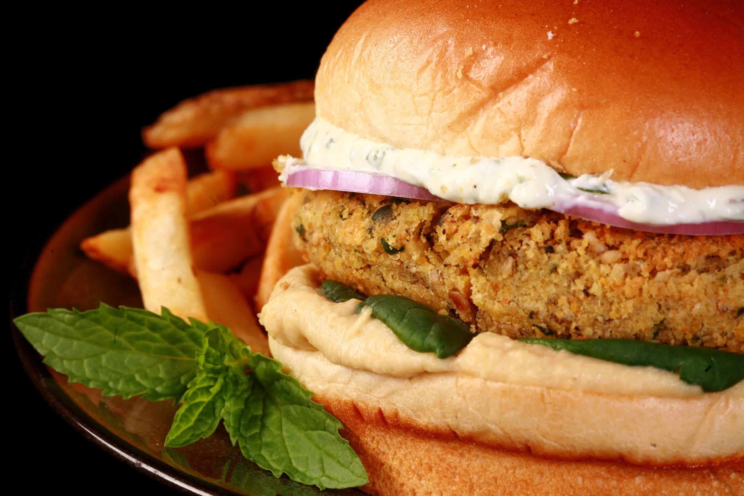 A dukkah spiced falafel burger with spinach, red onions, hummus, and labneh feta mint spread.
