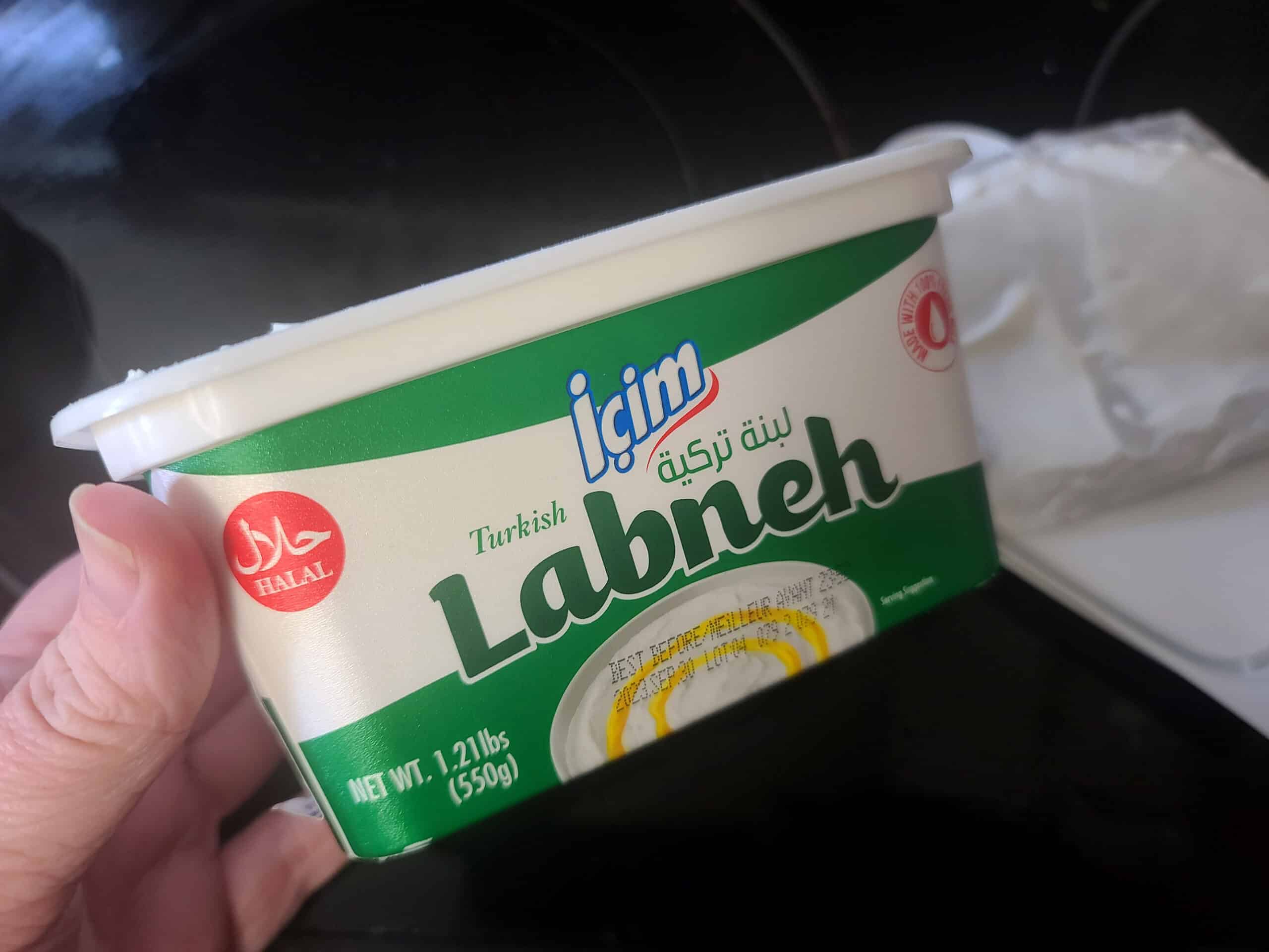 A hand holds a carton of labneh.