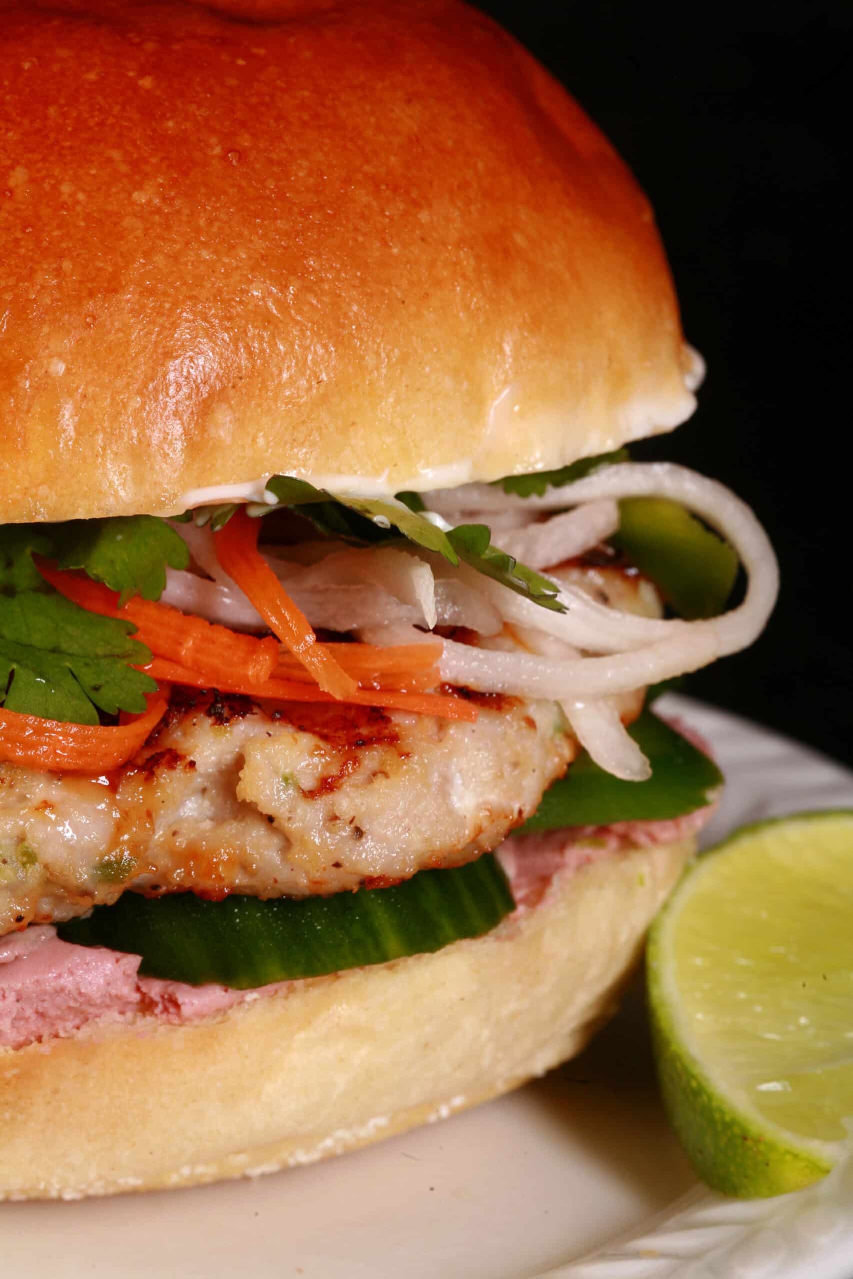 A lemongrass chicken banh mi burger, with cucumbers, pate, cilantro, jalapenos, and pickled root veggies.