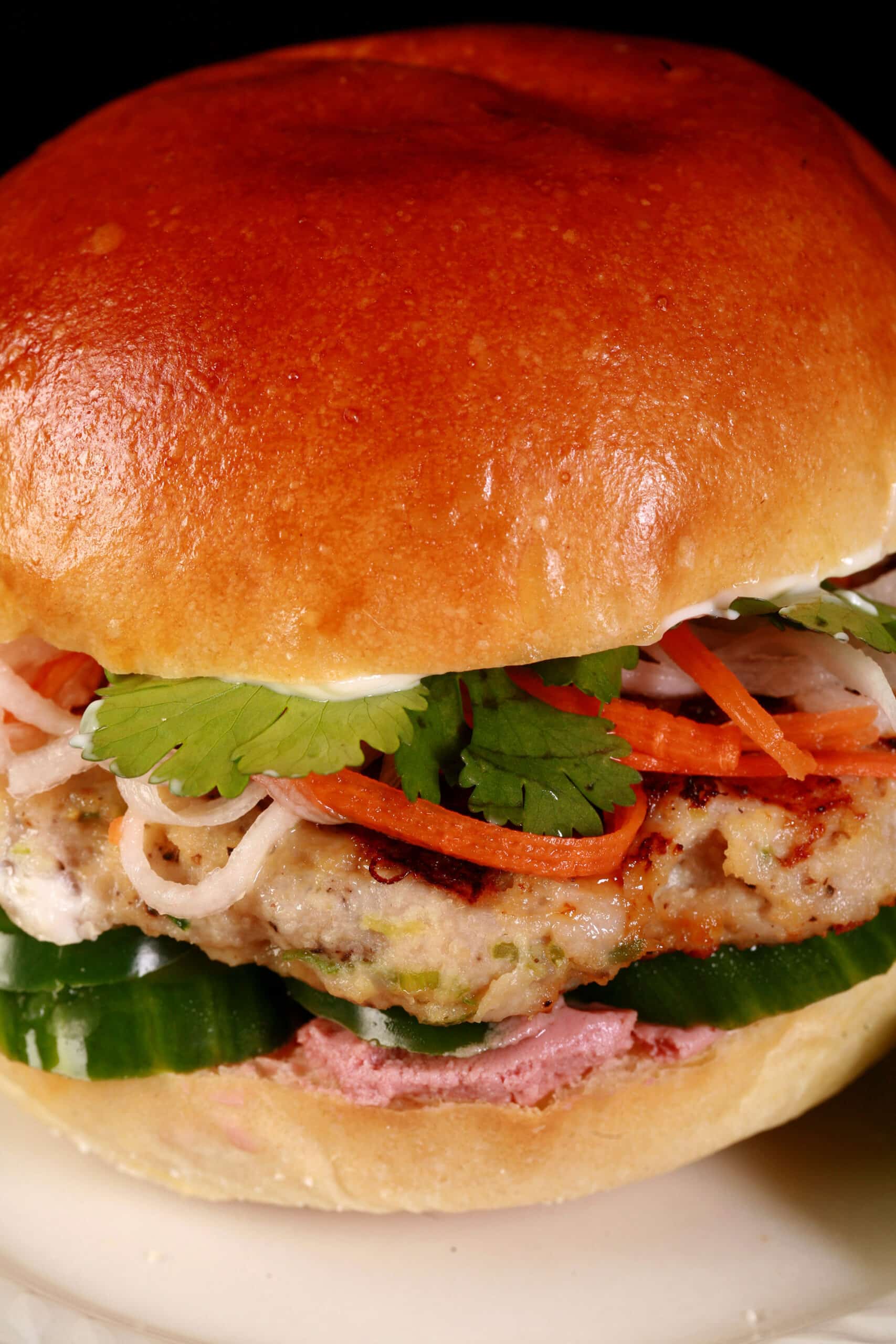 A lemongrass chicken banh mi burger, with cucumbers, pate, cilantro, jalapenos, and pickled root veggies.