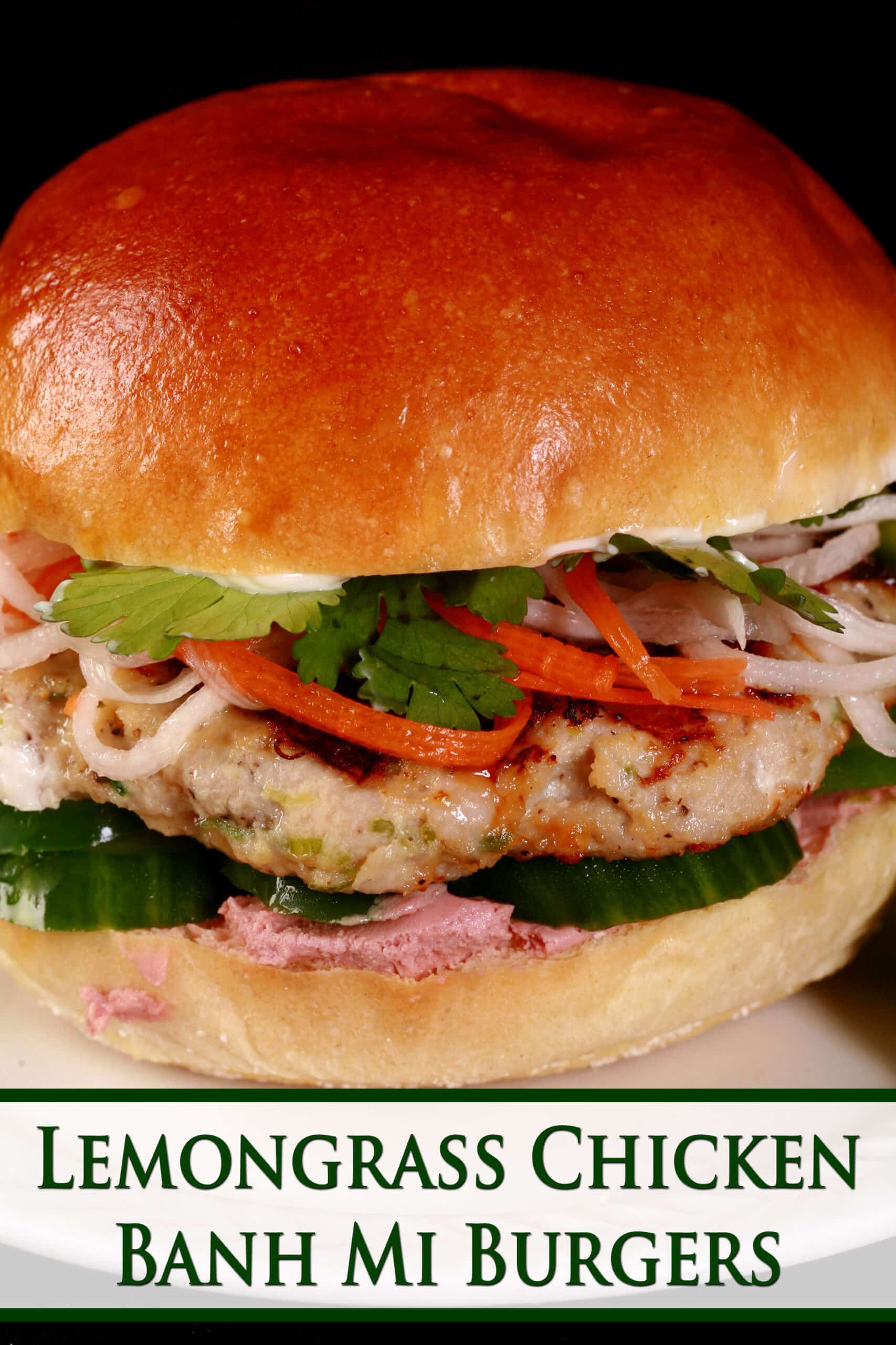 A fancy chicken burger with pickled veggies, cucumber slices, and more. Green text says lemongrass chicken banh mi burgers.