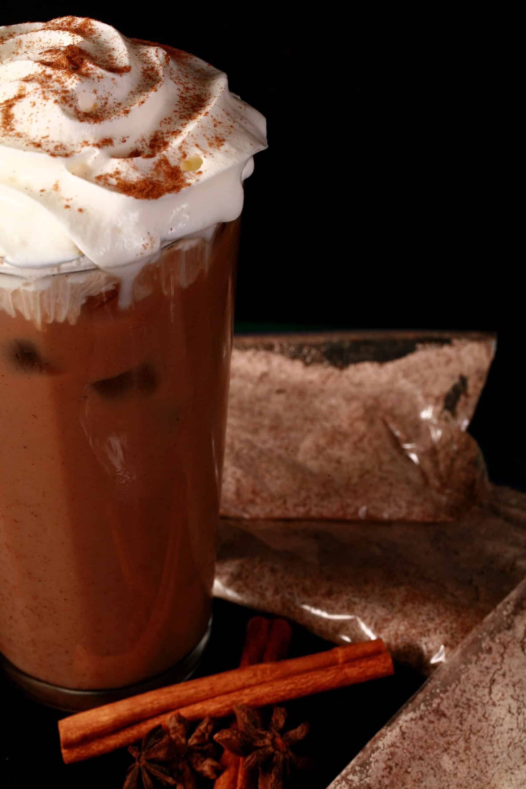 A glass of protein iced chai latte, with several bags of protein chai latte mix.