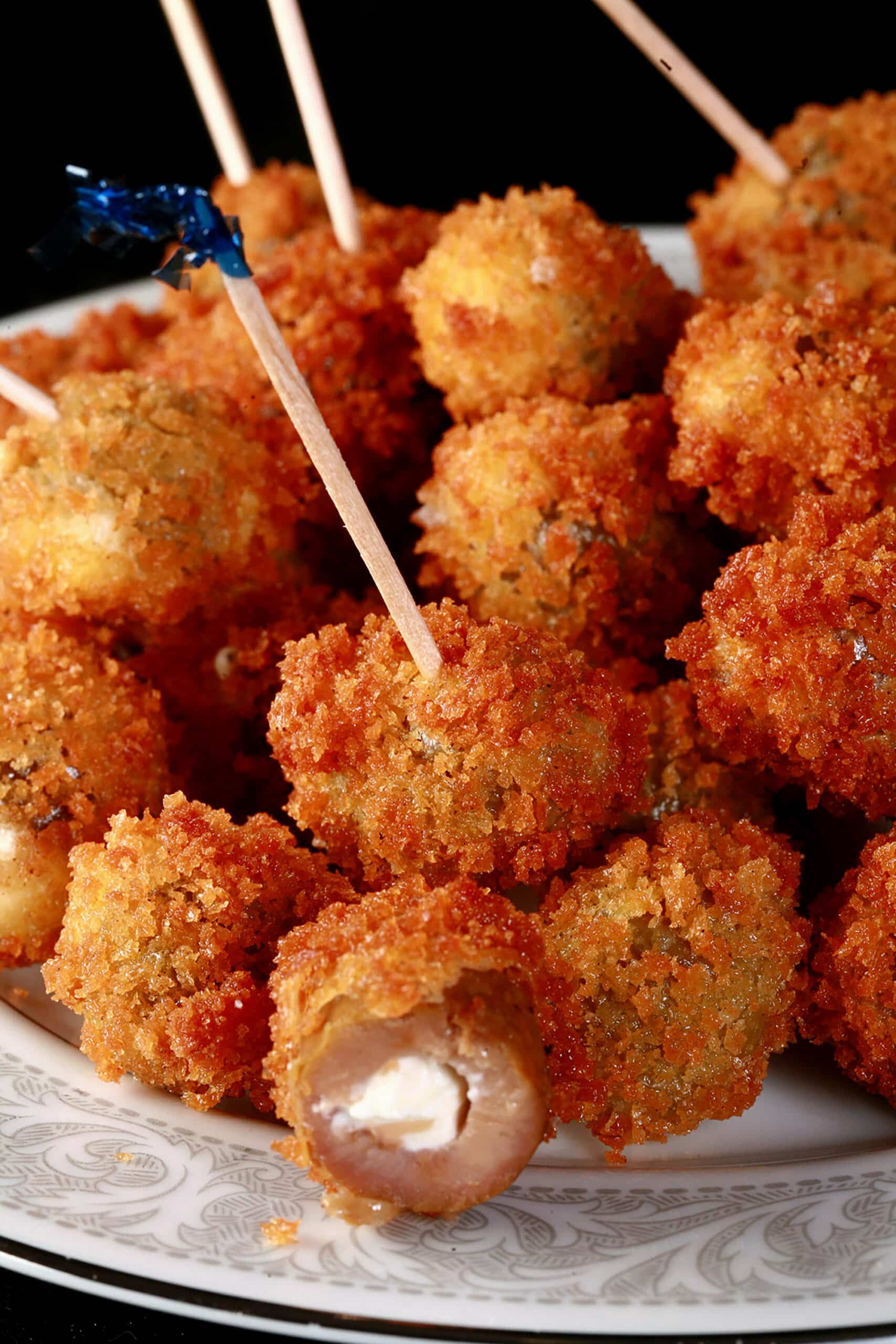 A pile of breaded deep fried olives on a plate. One is broken open to show it’s stuffed with a garlic cheese mixture.