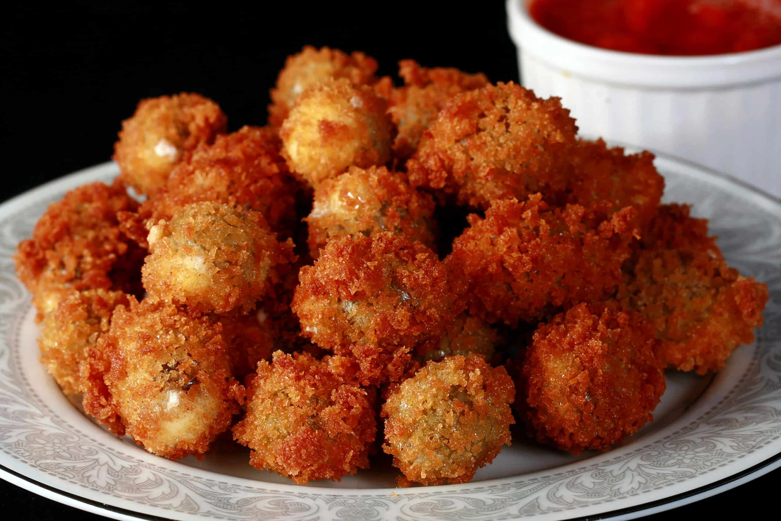 A plate of crispy deep fried olives with a small bowl of marinara sauce in the background.