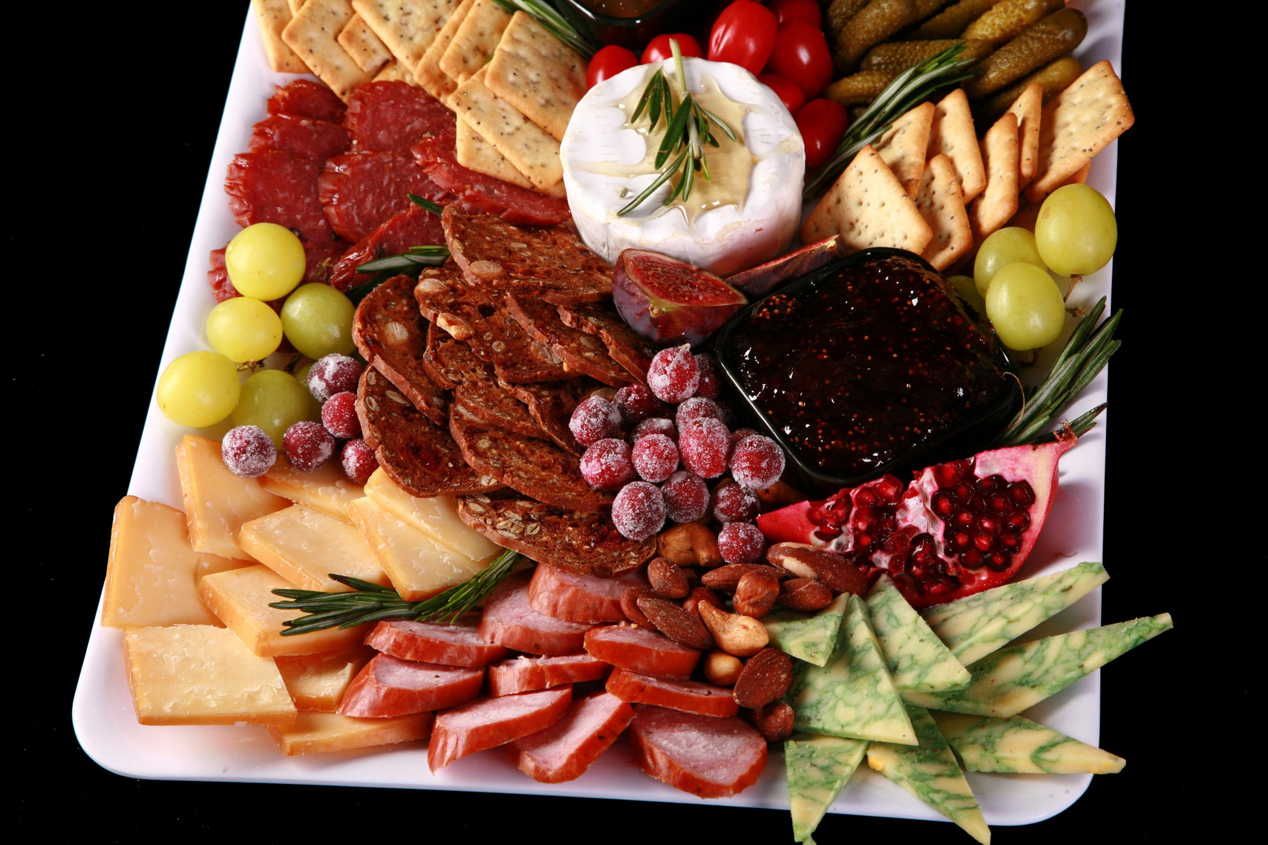 A festive christmas charcuterie platter with meats, cheeses, fruit and crackers in a variety of textures and jewel tone colours.