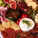 A festive christmas charcuterie board with meats, cheeses, fruit and crackers in a variety of textures and jewel tone colours.