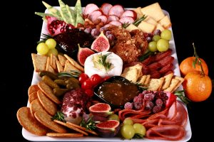 A festive christmas charcuterie platter with meats, cheeses, fruit and crackers in a variety of textures and jewel tone colours.