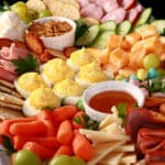 A pastel themed Easter Charcuterie board, with ham, turkey, cheeses, deviled eggs, mini eggs, baby carrots, and more.