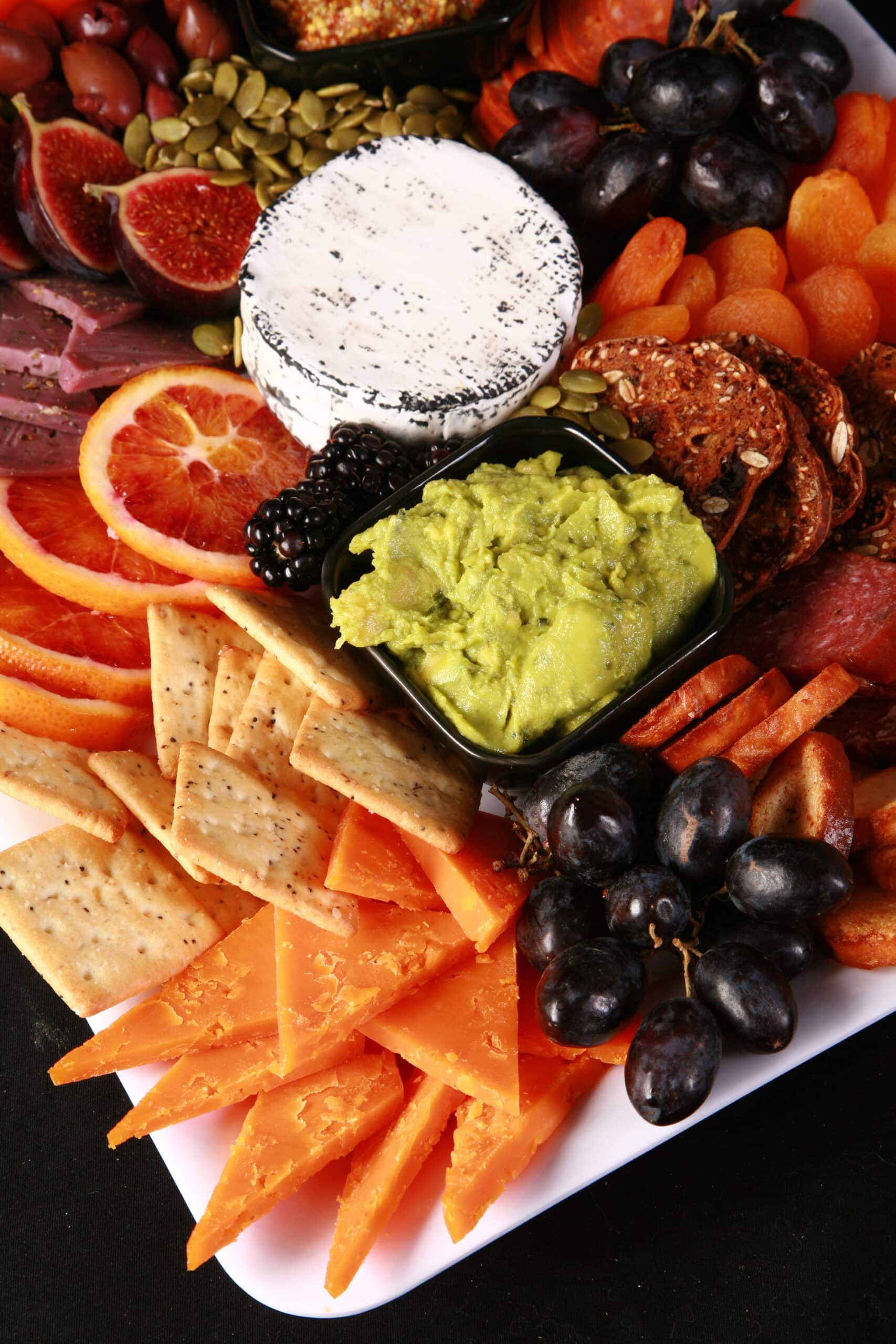 An elegant halloween charcuterie platter with jewel toned foods and skeleton hand accents.