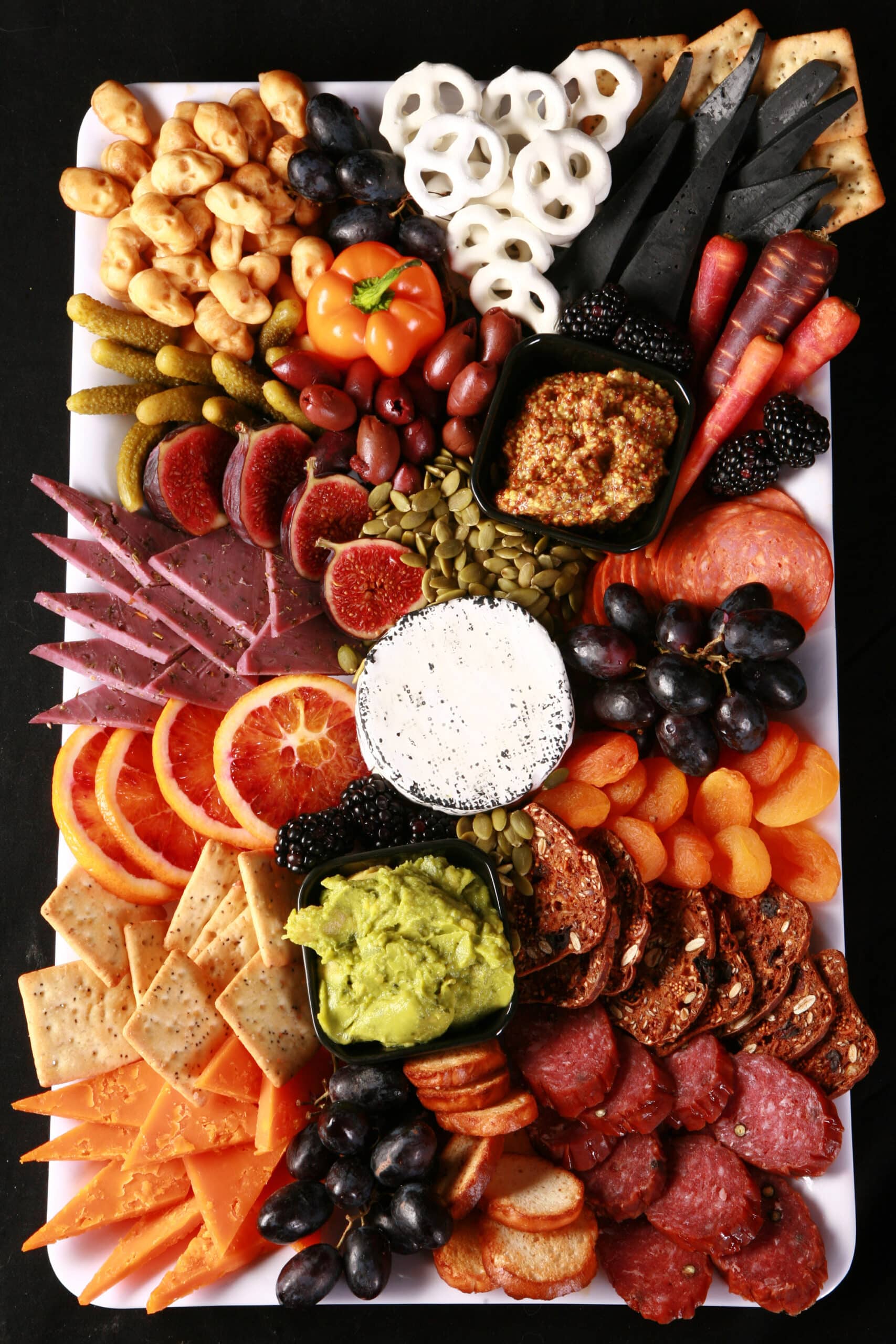 An spooky halloween charcuterie board with jewel toned foods and skeleton hand accents.