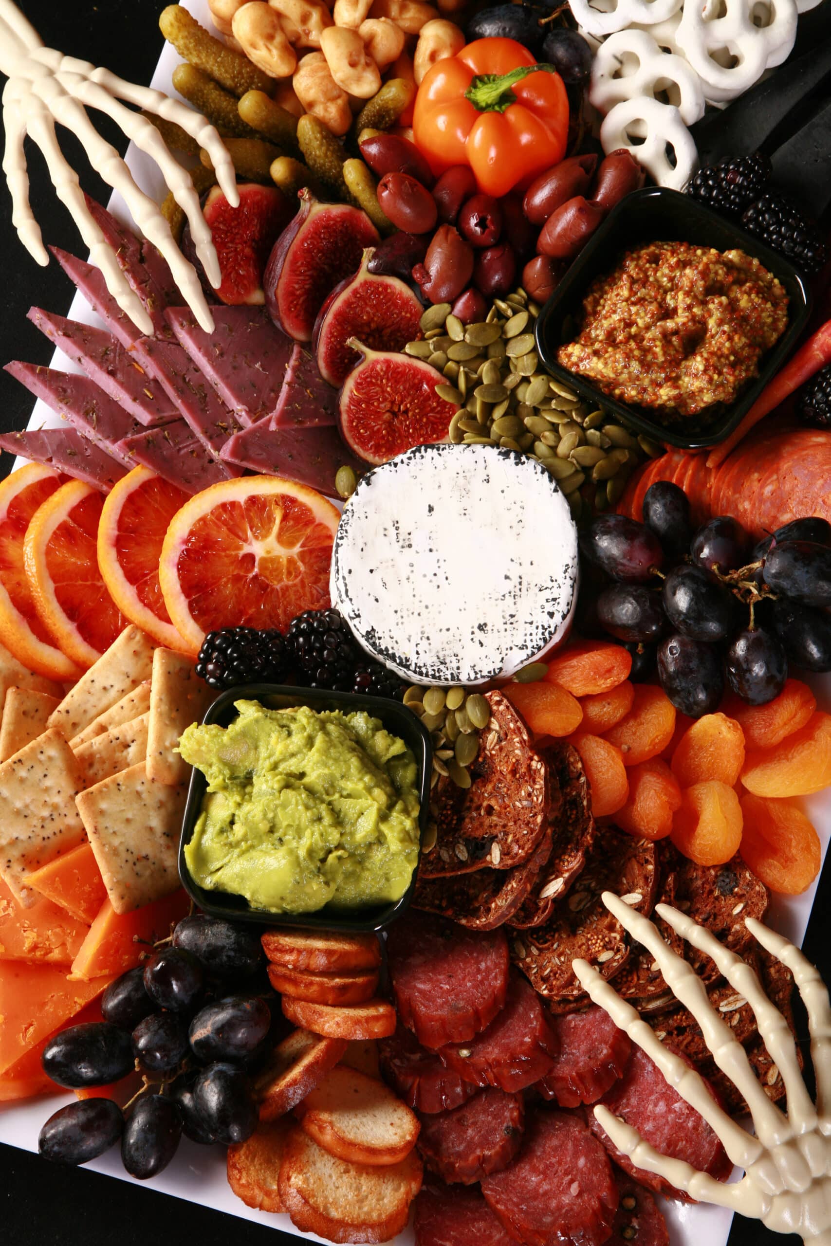 An elegant halloween charcuterie board with jewel toned foods and skeleton hand accents.