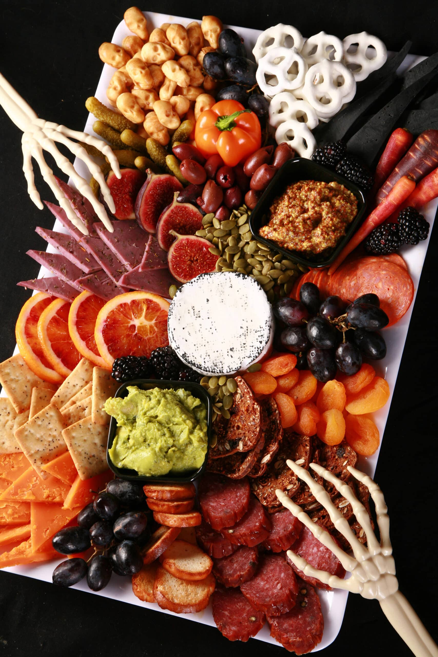 An spooky halloween charcuterie platter with jewel toned foods and skeleton hand accents.