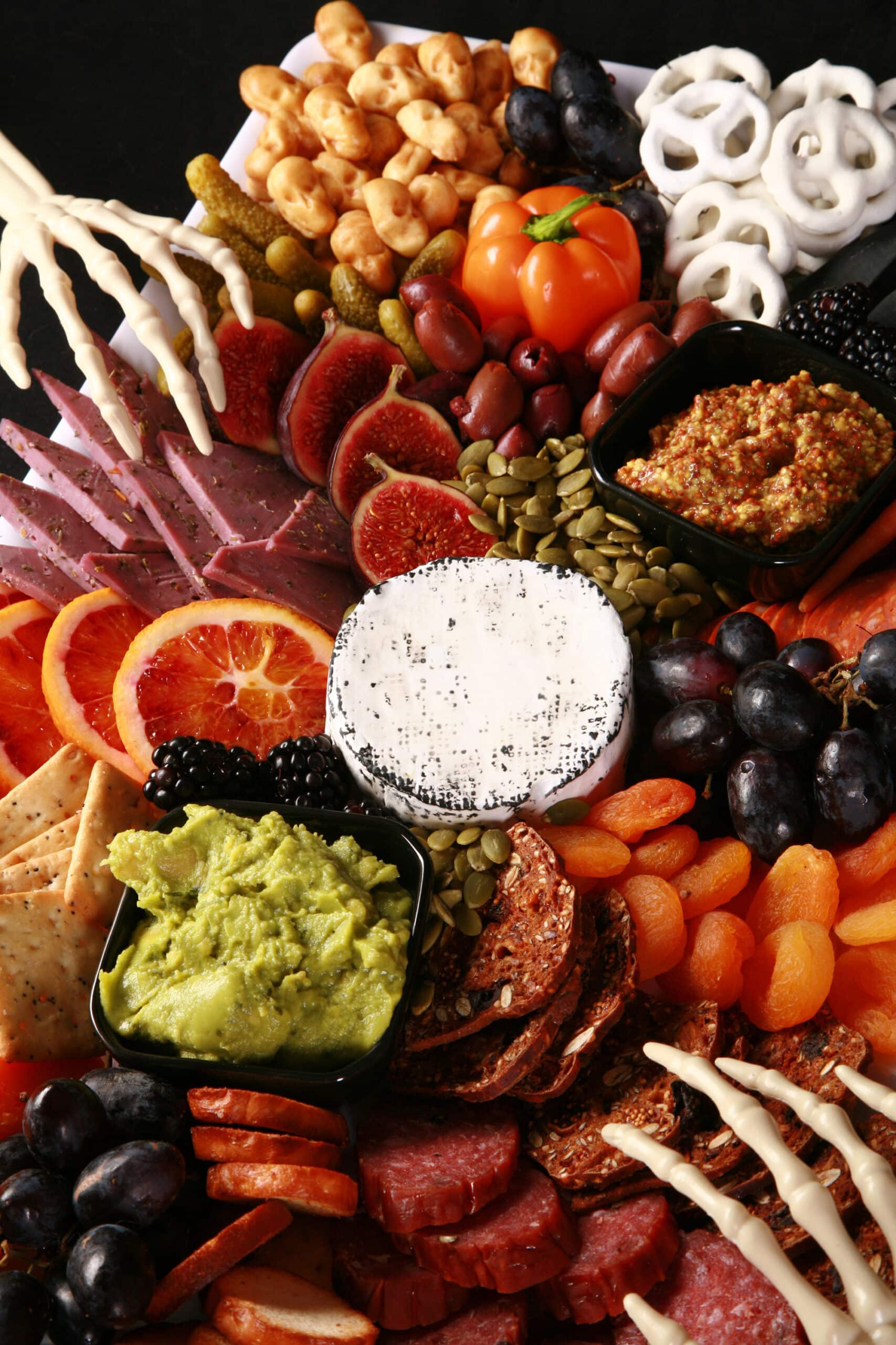 An elegant halloween charcuterie platter with jewel toned foods and skeleton hand accents.