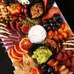 An elegant halloween charcuterie board with jewel toned foods and skeleton hand accents.