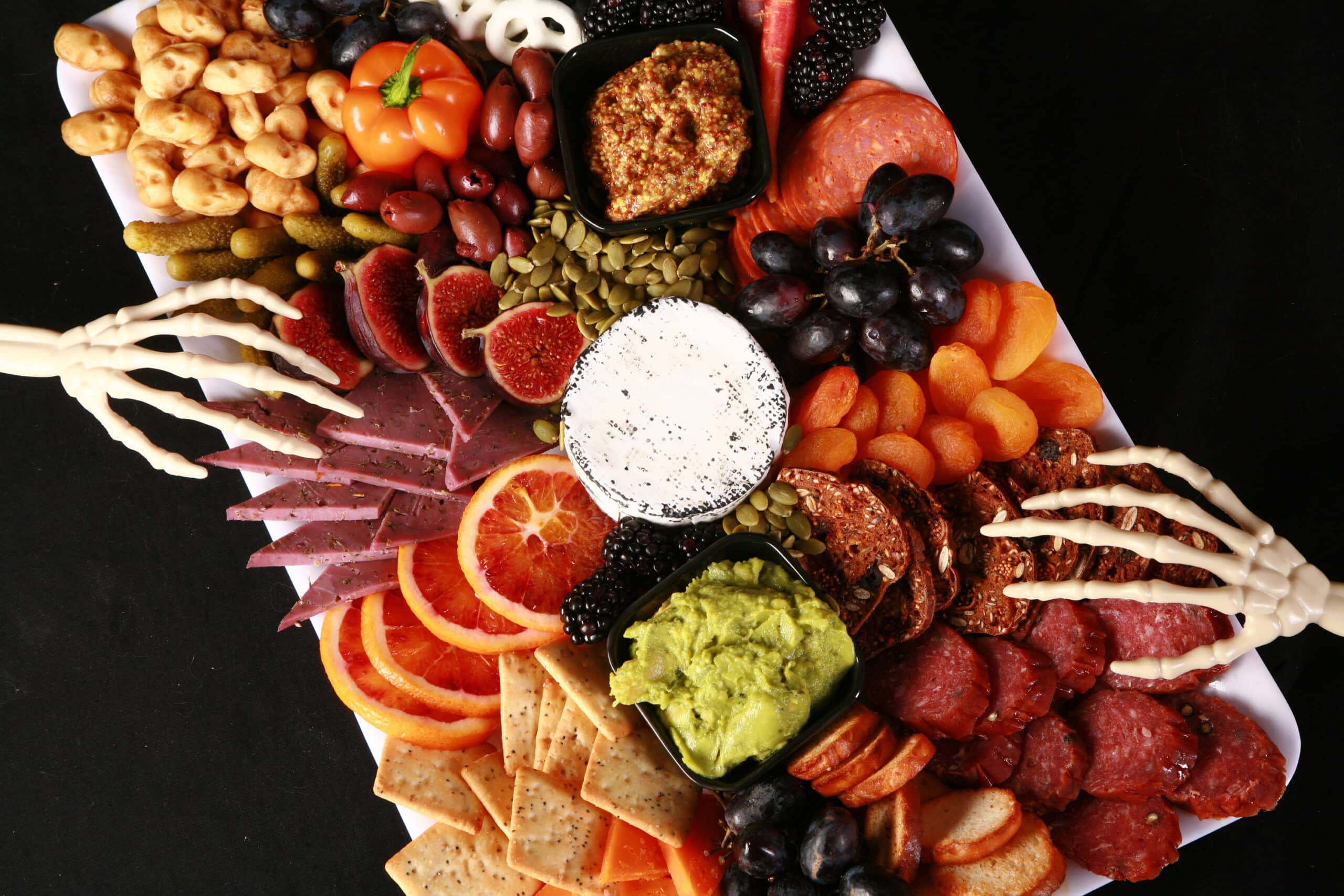 An elegant halloween charcuterie board with jewel toned foods and skeleton hand accents.