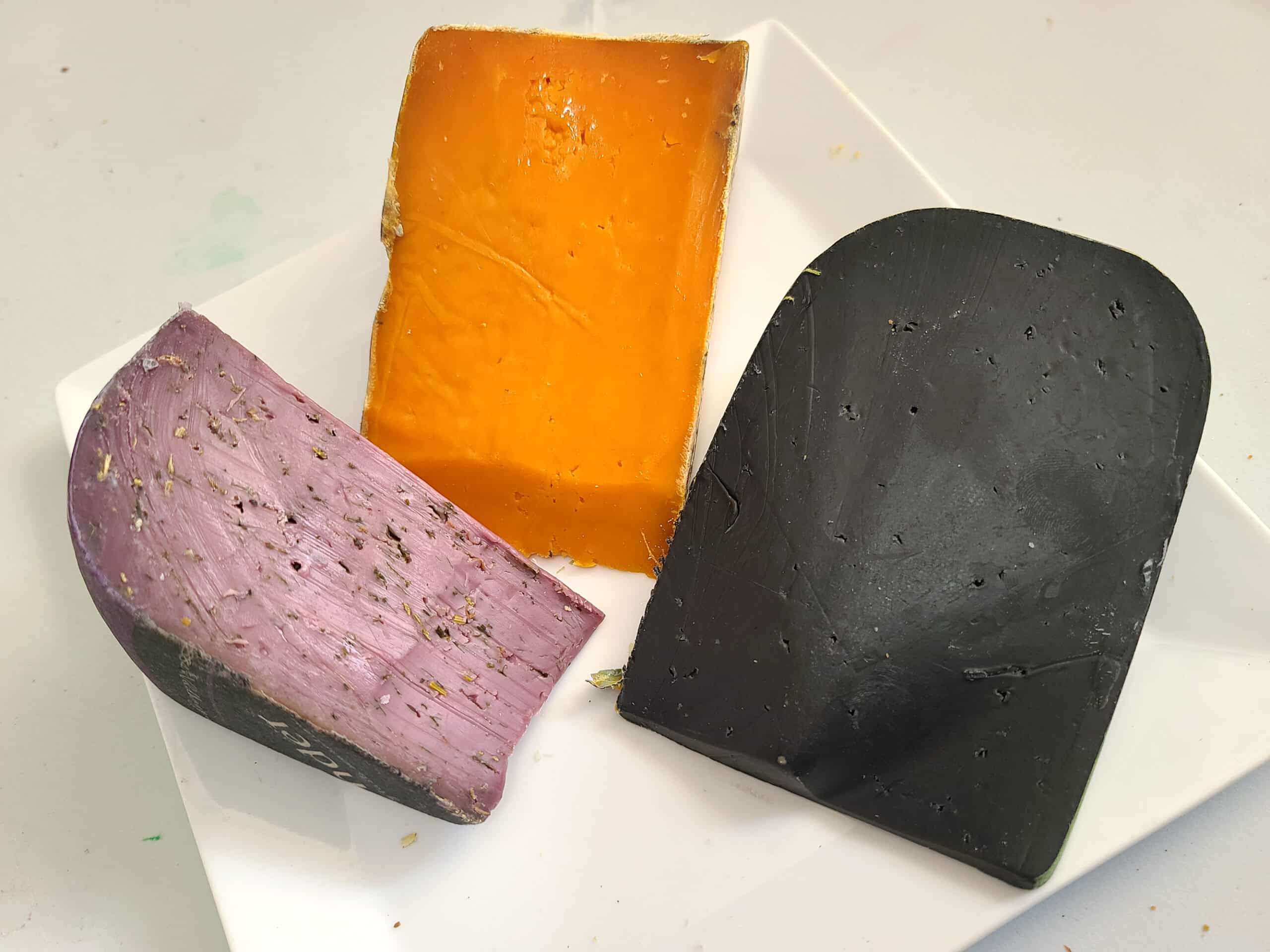 Purple, orange, and black cheeses on a cutting board.