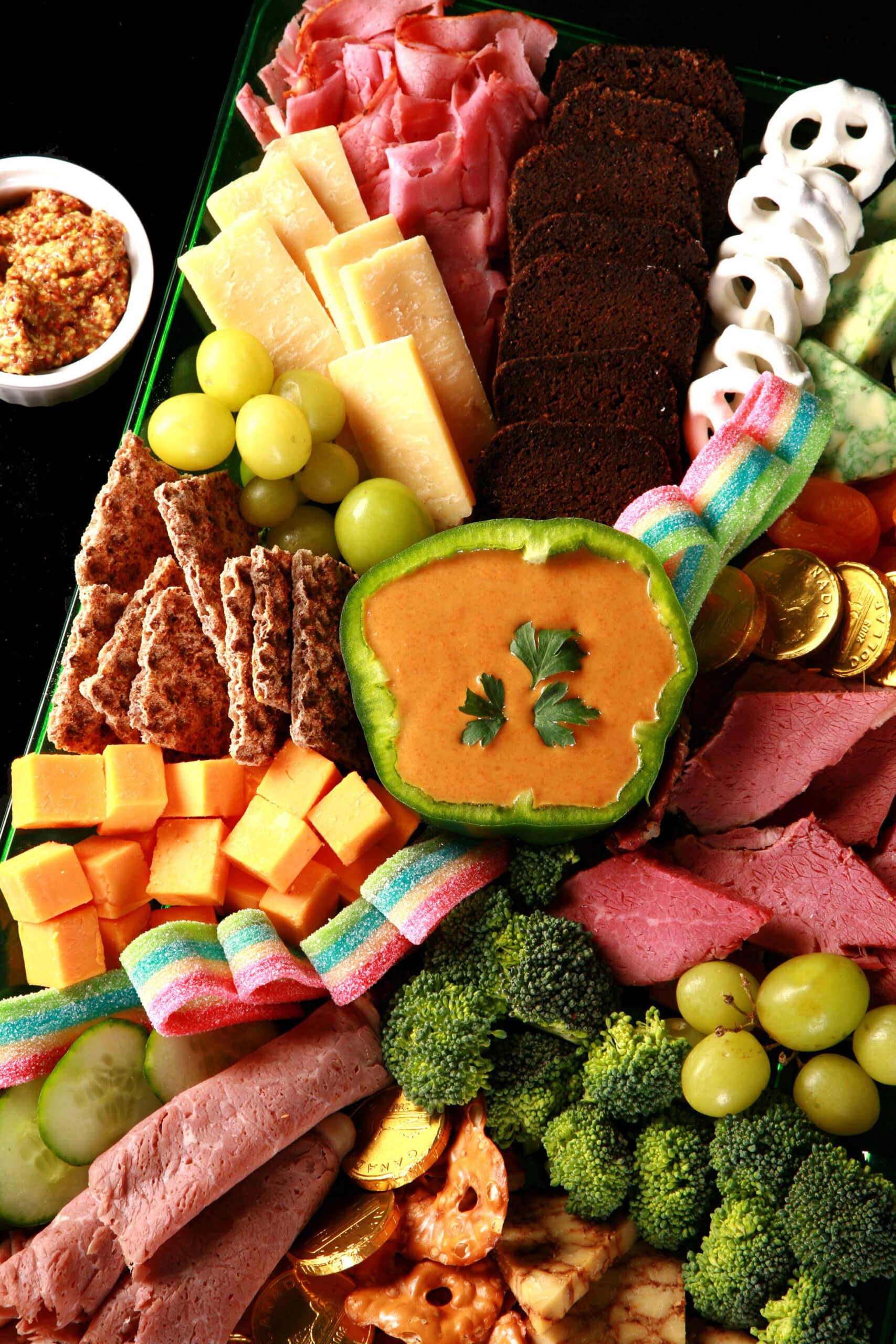 A St Patrick's Day Charcuterie board with Irish cheeses, Guinness Cheese Dip, Gold chocolate coins, rainbow candy, and more.