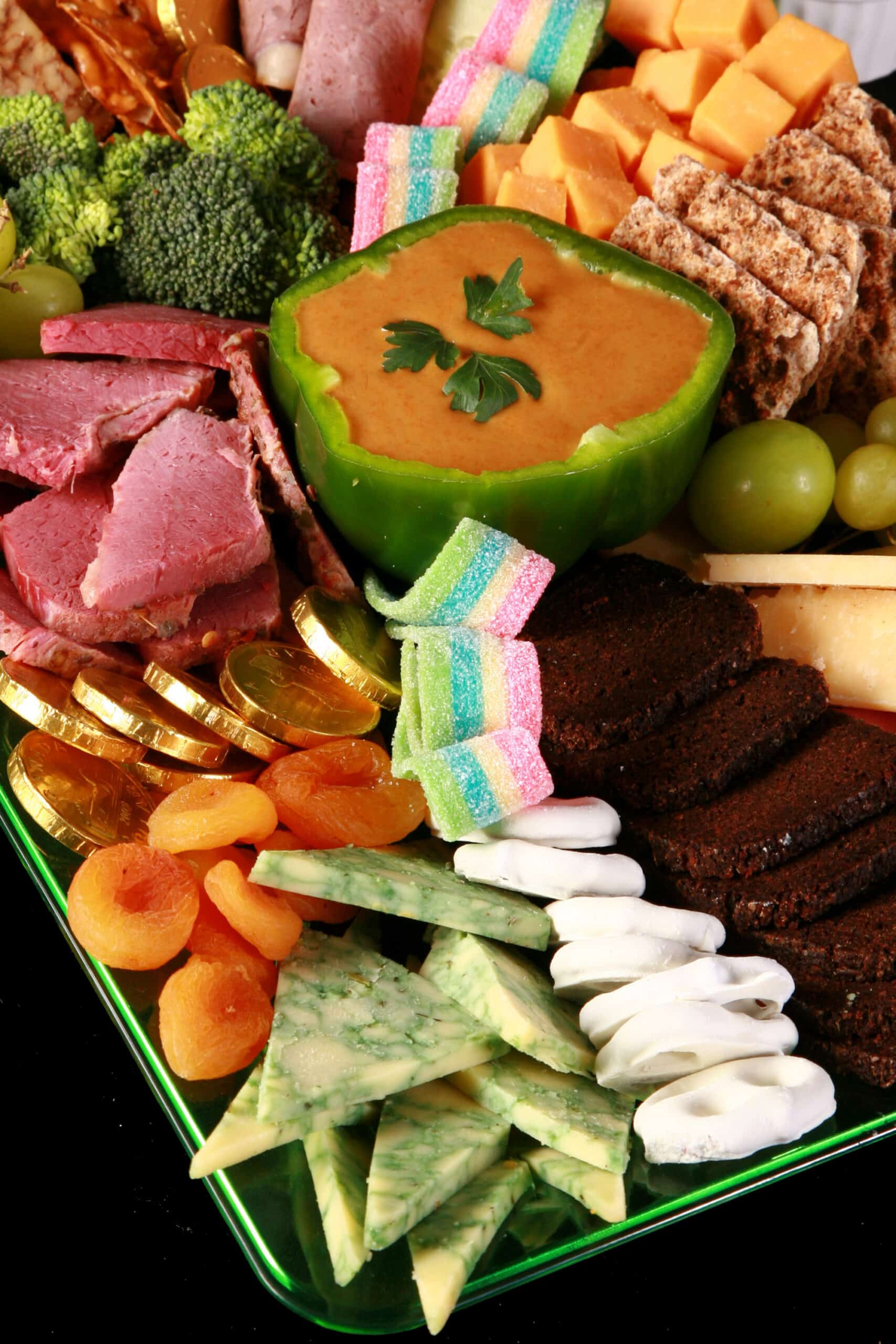 A St Patrick's Day Charcuterie board with Irish cheeses, Guinness Cheese Dip, Gold chocolate coins, rainbow candy, and more.