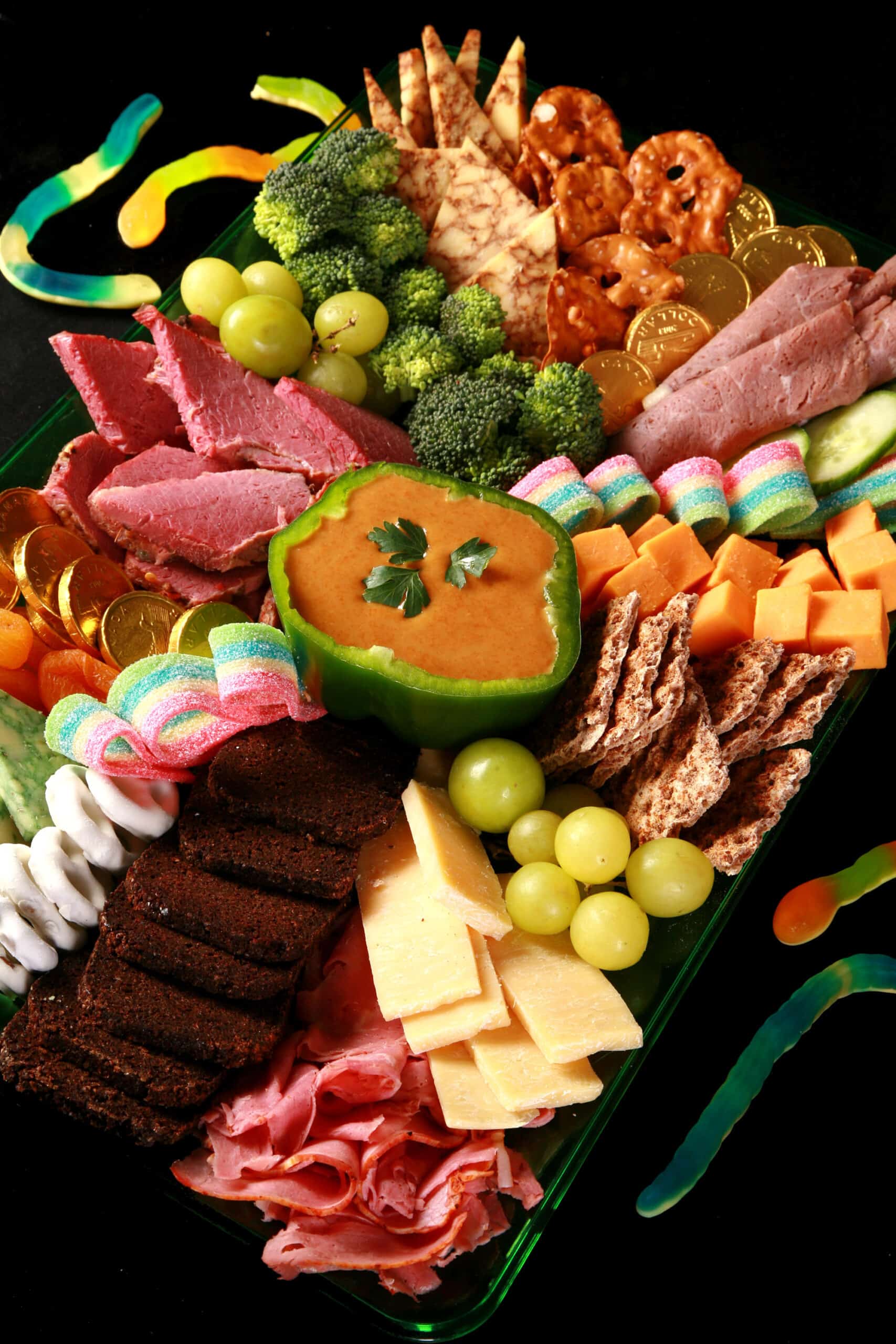 A St Patrick's Day Charcuterie board with Irish cheeses, Guinness Cheese Dip, Gold chocolate coins, rainbow candy, and more.