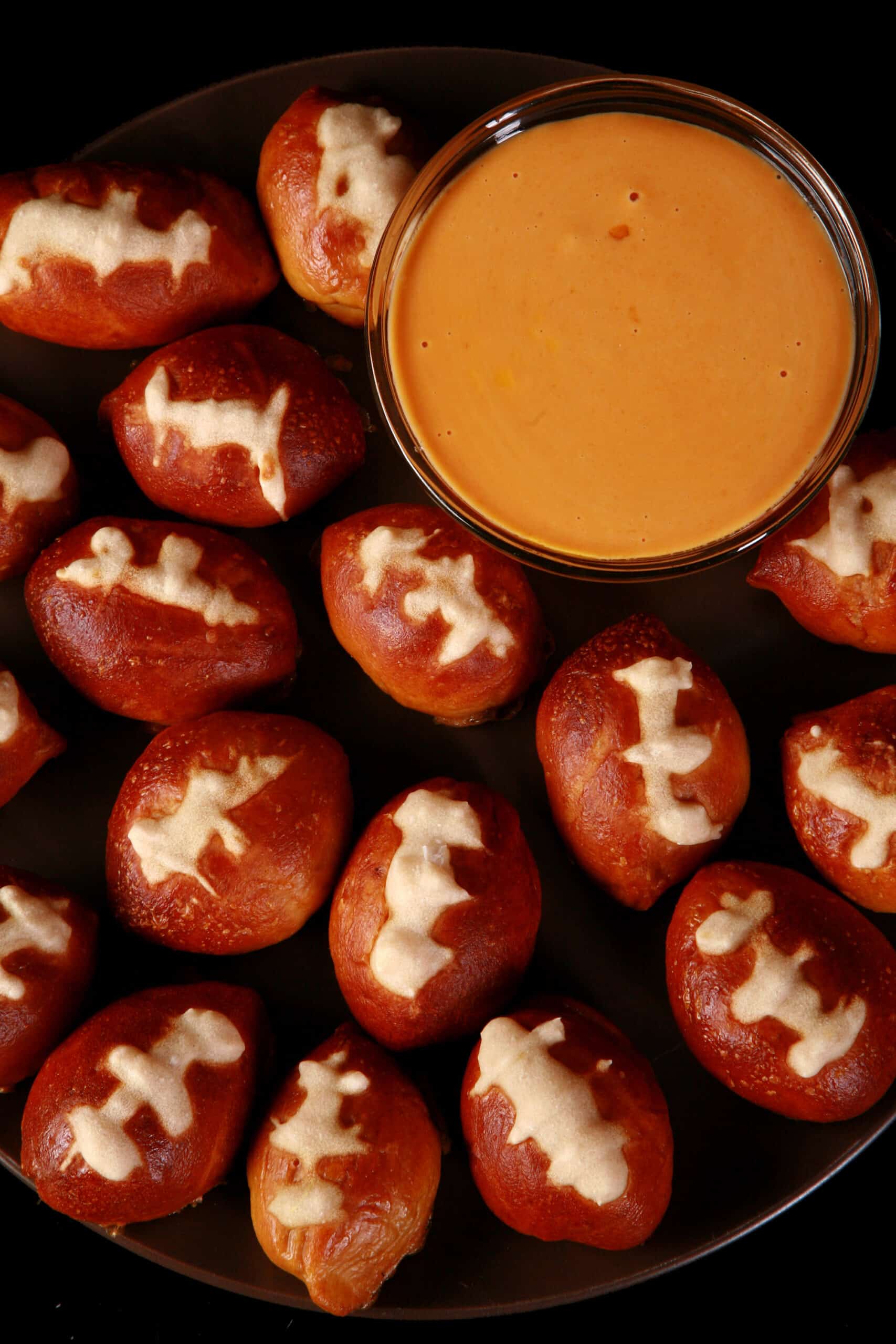 A plate of mini football soft pretzel bites, with a bowl of hot cheese dip.