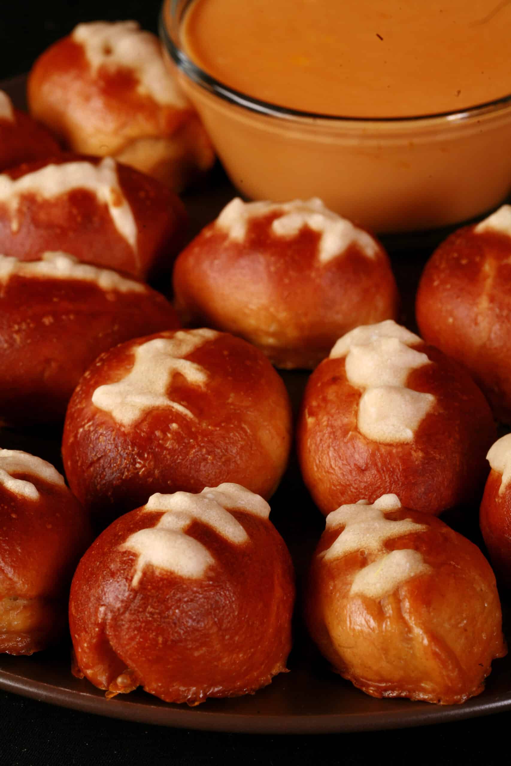 A plate of mini football pretzel bites, with a bowl of hot cheese dip.