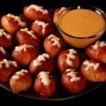A plate of mini football soft pretzel bites, with a bowl of hot cheese dip.
