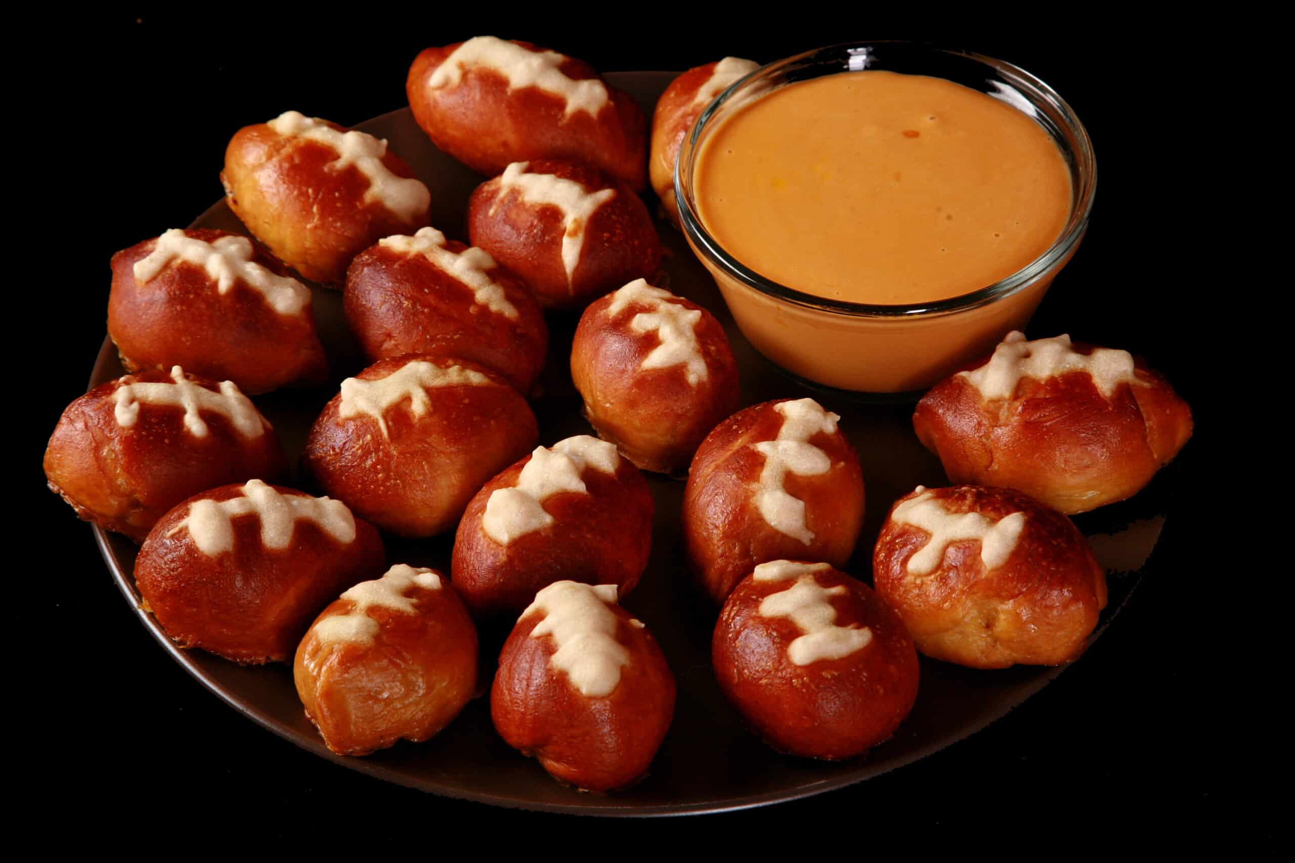 A plate of mini football soft pretzel bites, with a bowl of hot cheese dip.