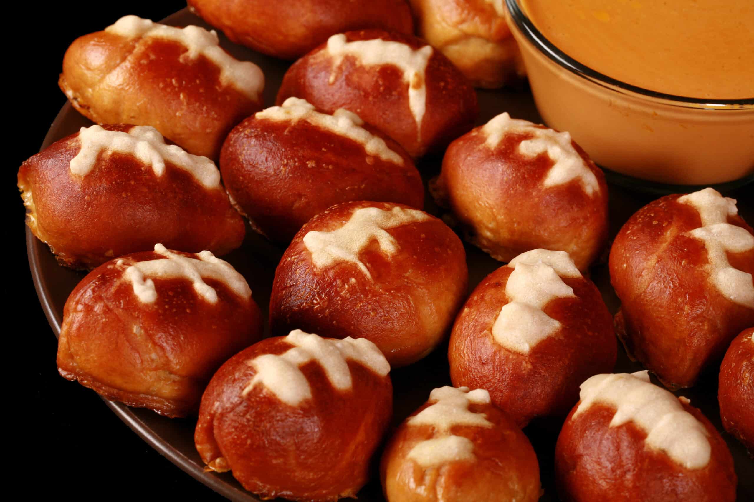 A plate of mini football pretzel bites, with a bowl of hot cheese dip.