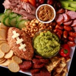 A game day charcuterie platter, with a football shaped cheese ball, football mini pretzels, guacamole, beer cheese dip, meats, Guinness cheese, corn nuts, pretzels, and more.