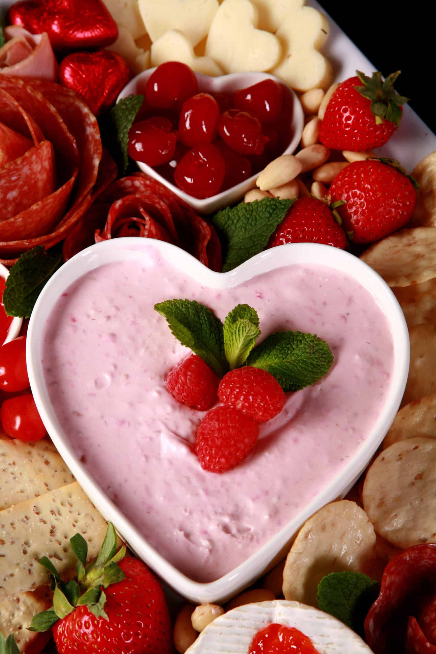 A close up photo of a valentine’s day charcuterie board, focused on a bowl of raspberry cheesecake dip.