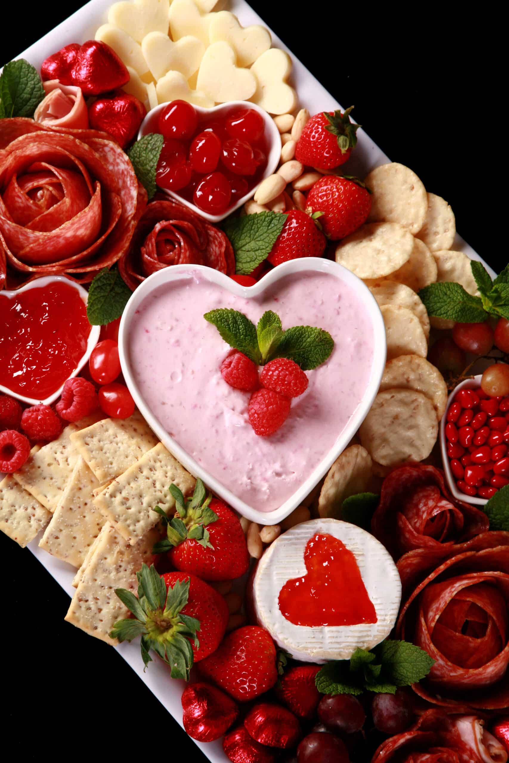 A valentine’s charcuterie board, with heart shaped cheese slices, salami roses, foil wrapped chocolates, strawberries, and more.