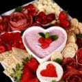 A valentine charcuterie board, with heart shaped cheese slices, salami roses, foil wrapped chocolates, strawberries, and more.