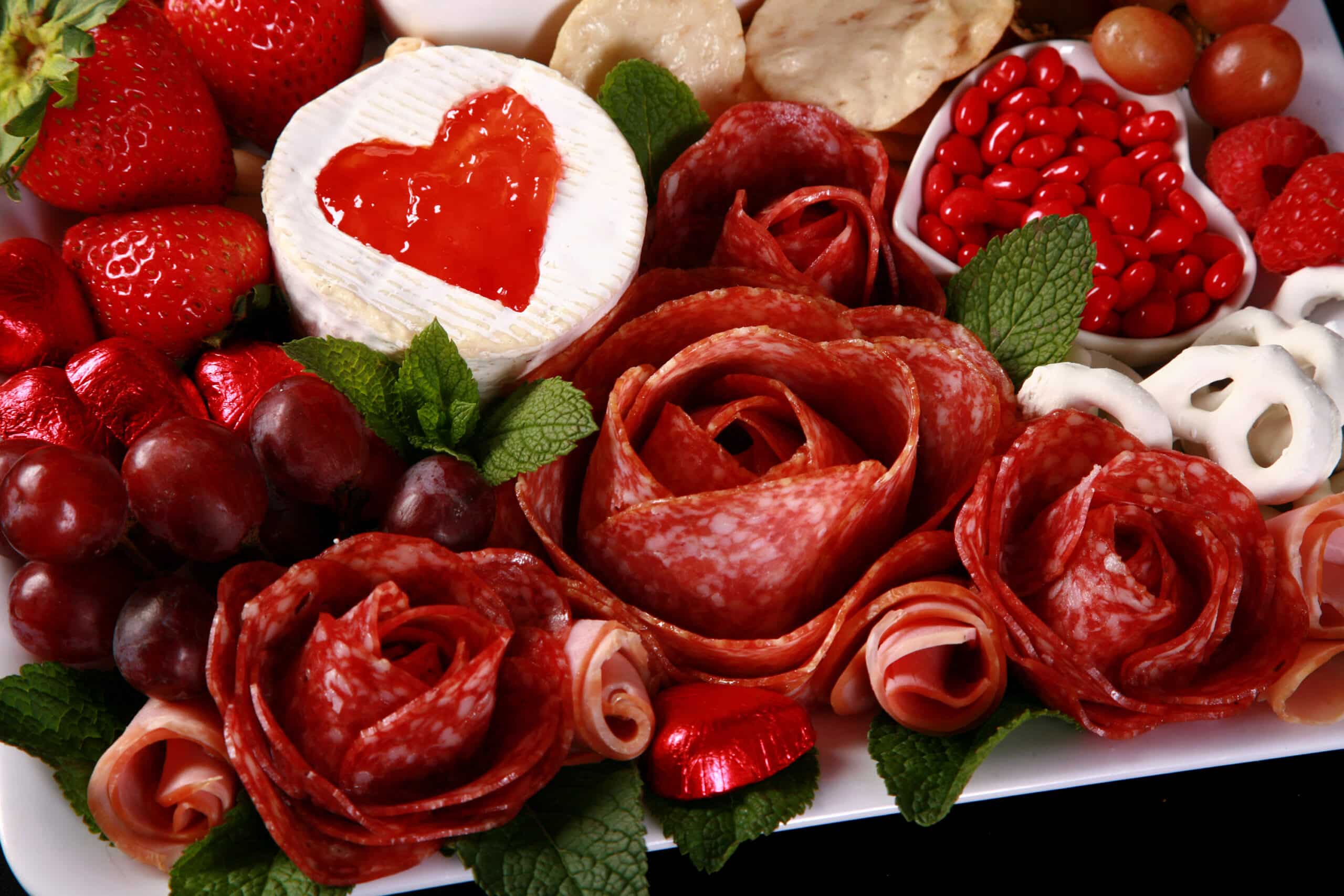 A valentine’s charcuterie board, with heart shaped cheese slices, salami roses, foil wrapped chocolates, strawberries, and more.