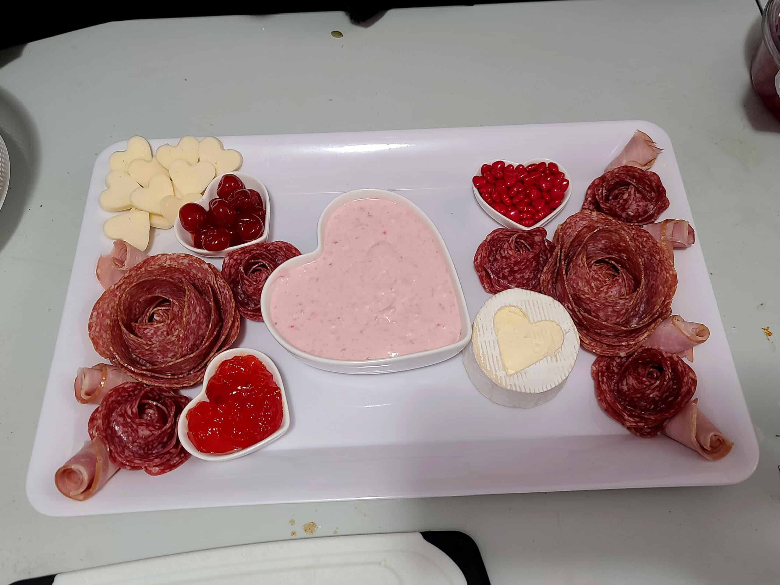 The start of a valentine’s charcuterie board, with salami roses and a few heart shaped bowls placed.