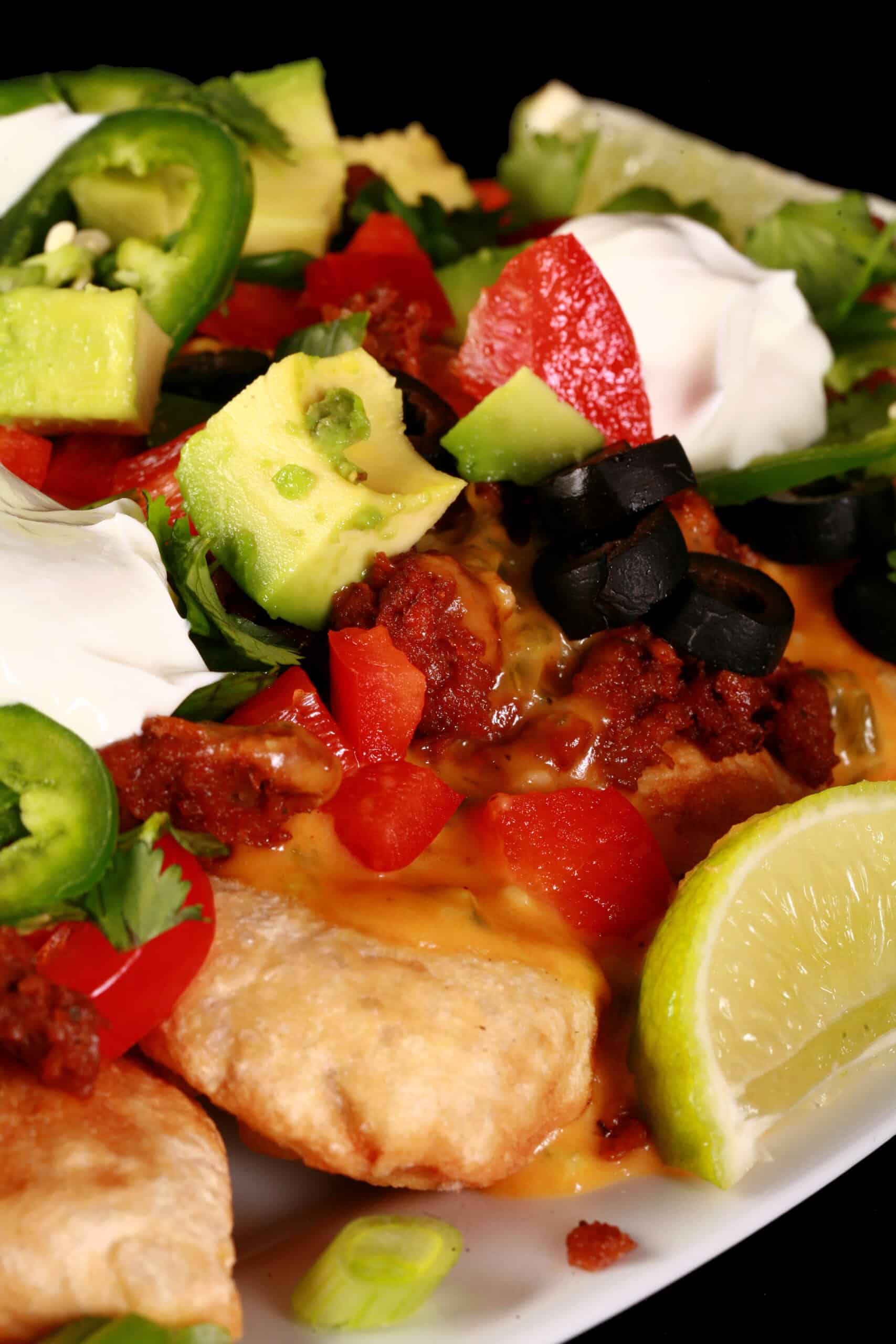 A plate of loaded pierogi nachos - deep fried perogies topped with jalapeno cheese sauce, nacho meat, and other toppings.