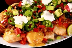 A plate of loaded perogy nachos - deep fried pierogi topped with jalapeno cheese sauce, nacho meat, and other toppings.