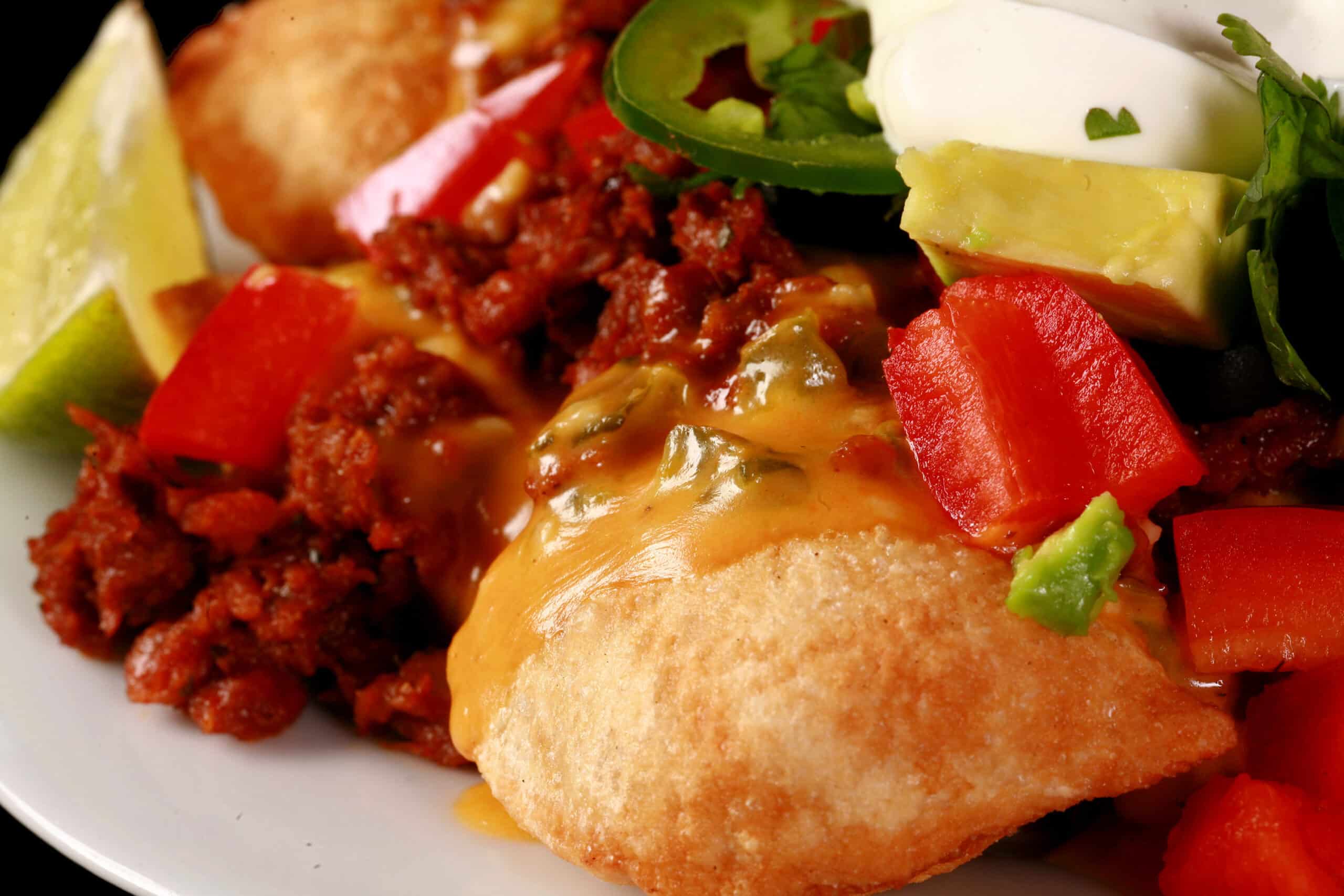 A plate of loaded pierogi nachos - deep fried perogies topped with jalapeno cheese sauce, nacho meat, and other toppings.