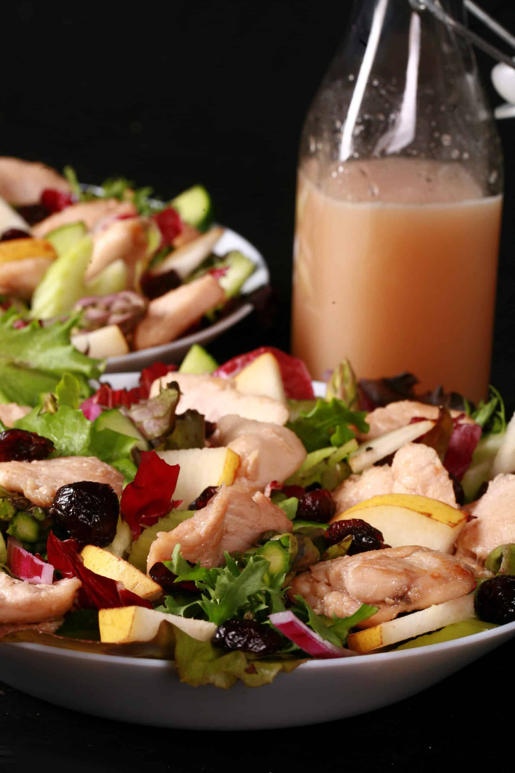 2 bowls of balsamic chicken salad with cranberries and pears, as well as a bottle of cranberry-pear white balsamic vinaigrette.