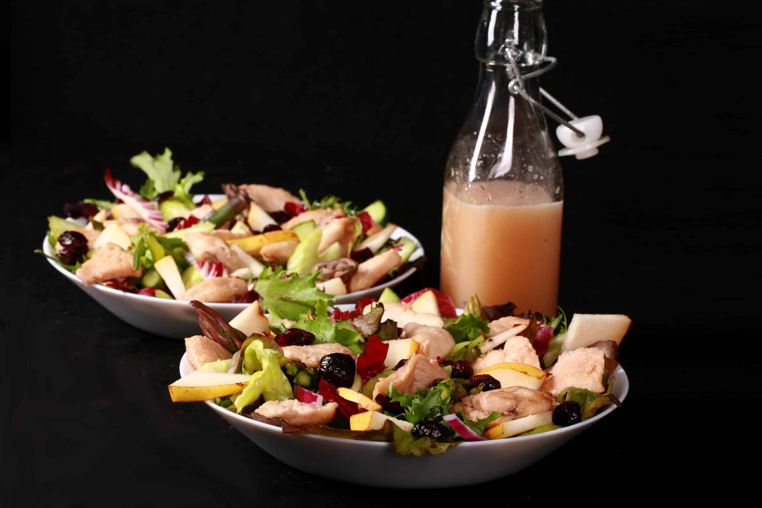 2 bowls of balsamic chicken salad with cranberries and pears, as well as a bottle of cranberry-pear white balsamic vinaigrette.