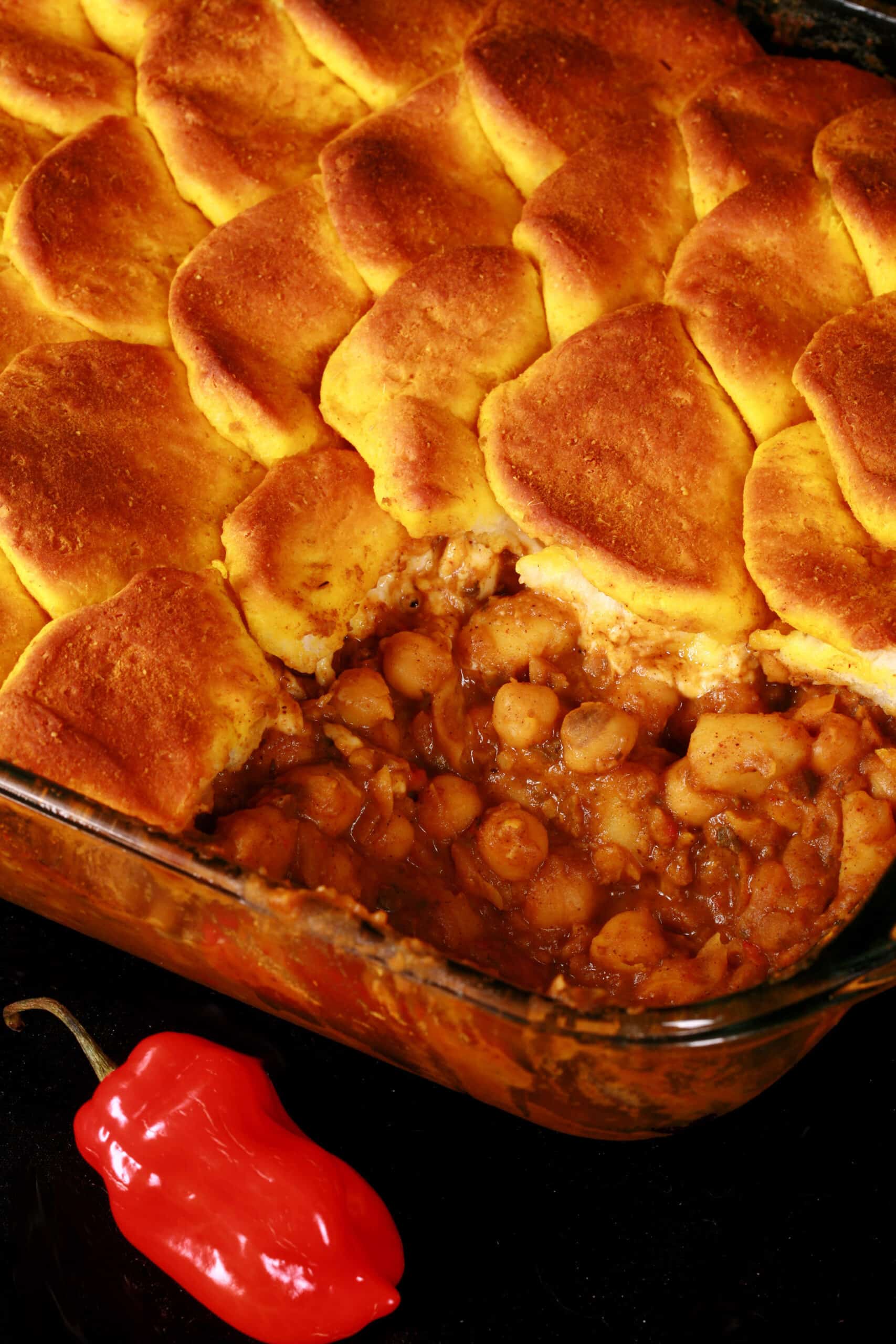 A serving of doubles casserole - a carribean inspired hotdish with a spiced chickpea and potato filling, topped with spiced butter brushed biscuits.