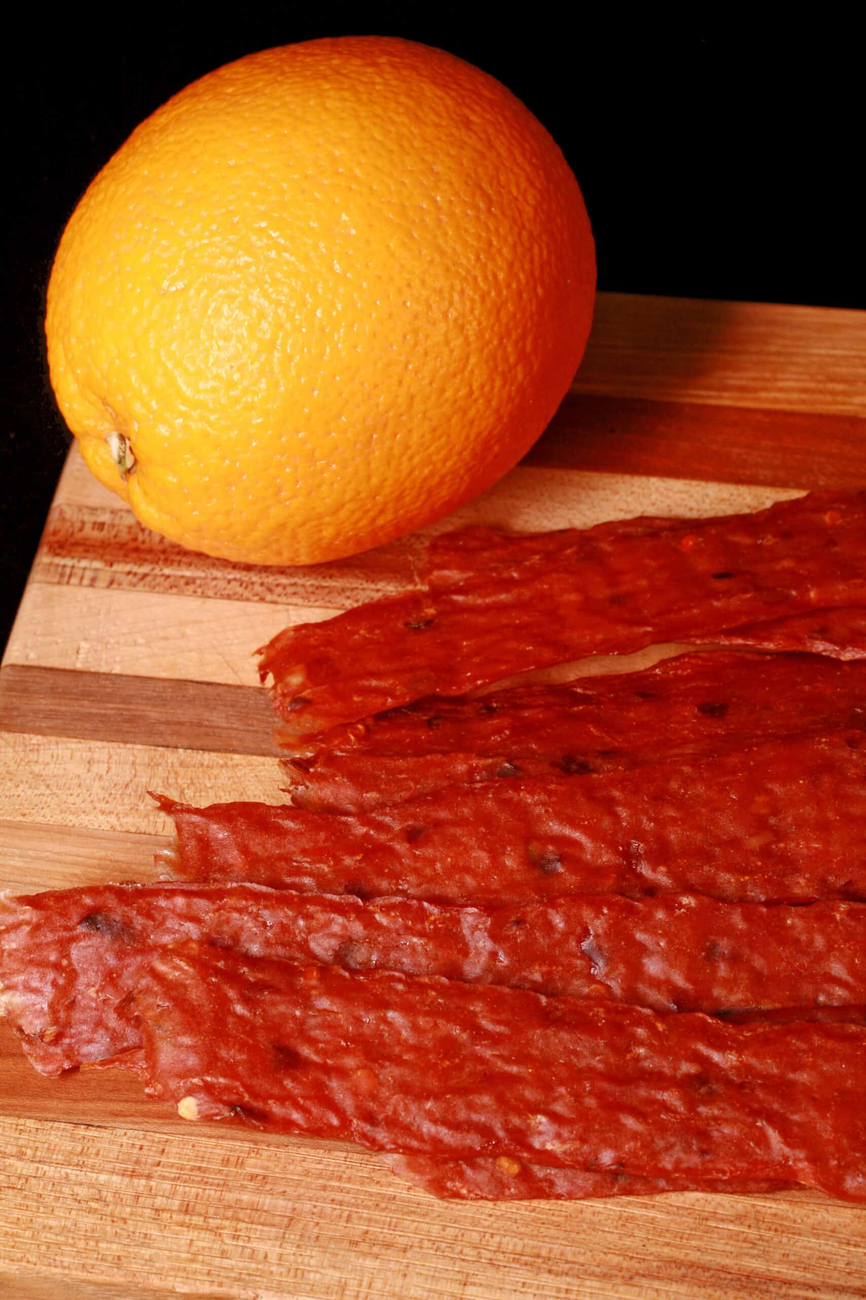 Several strips of spicy orange chicken jerky on a cutting board.