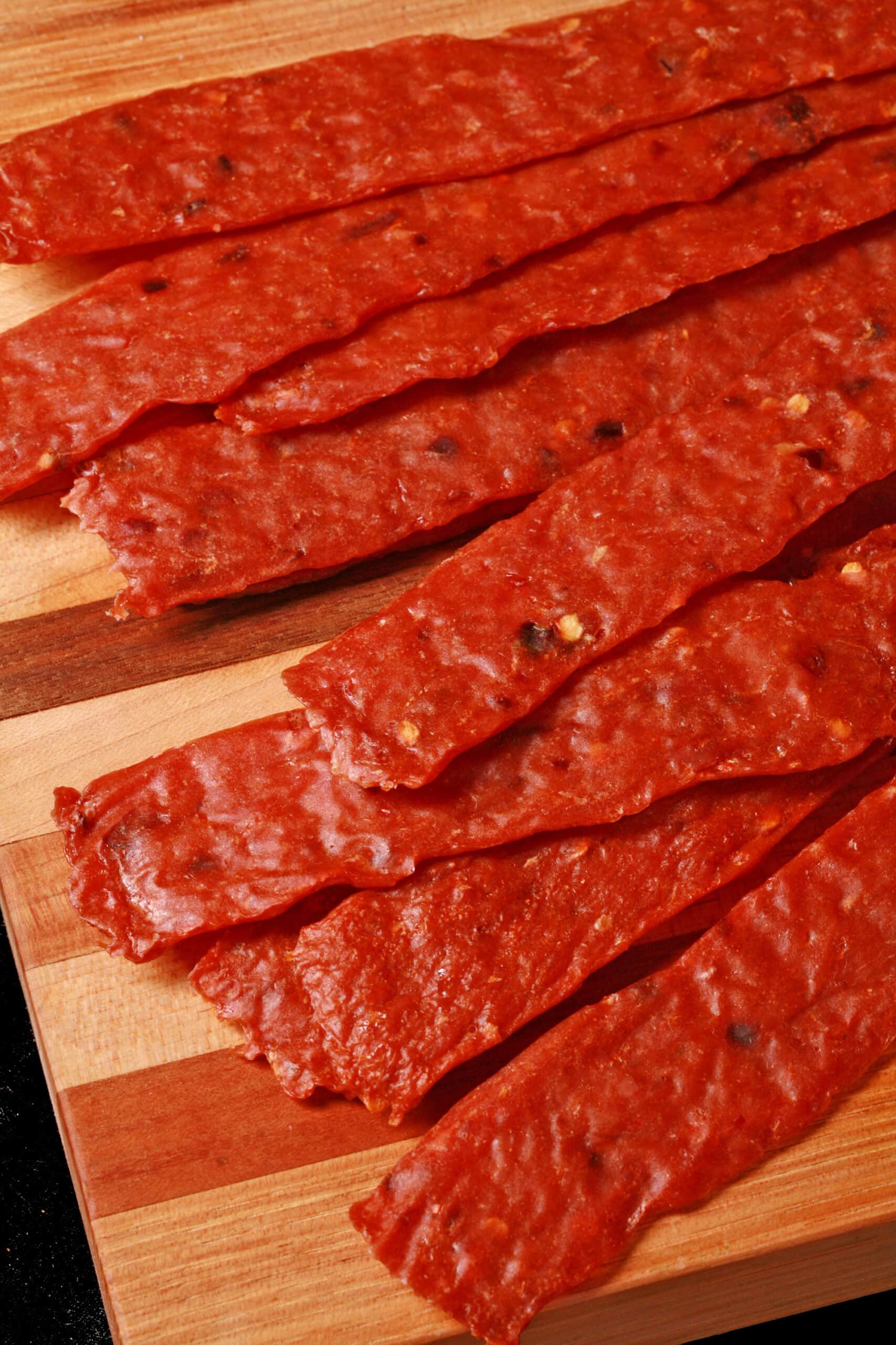 Several strips of spicy orange chicken jerky on a cutting board.