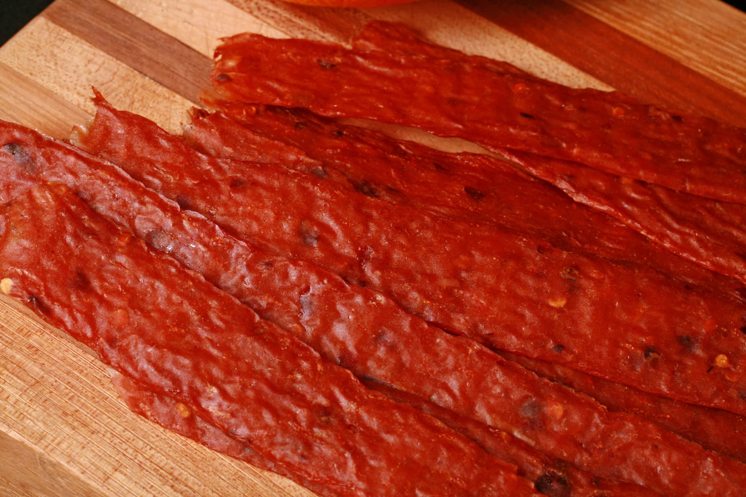 Several strips of spicy orange chicken jerky on a cutting board.