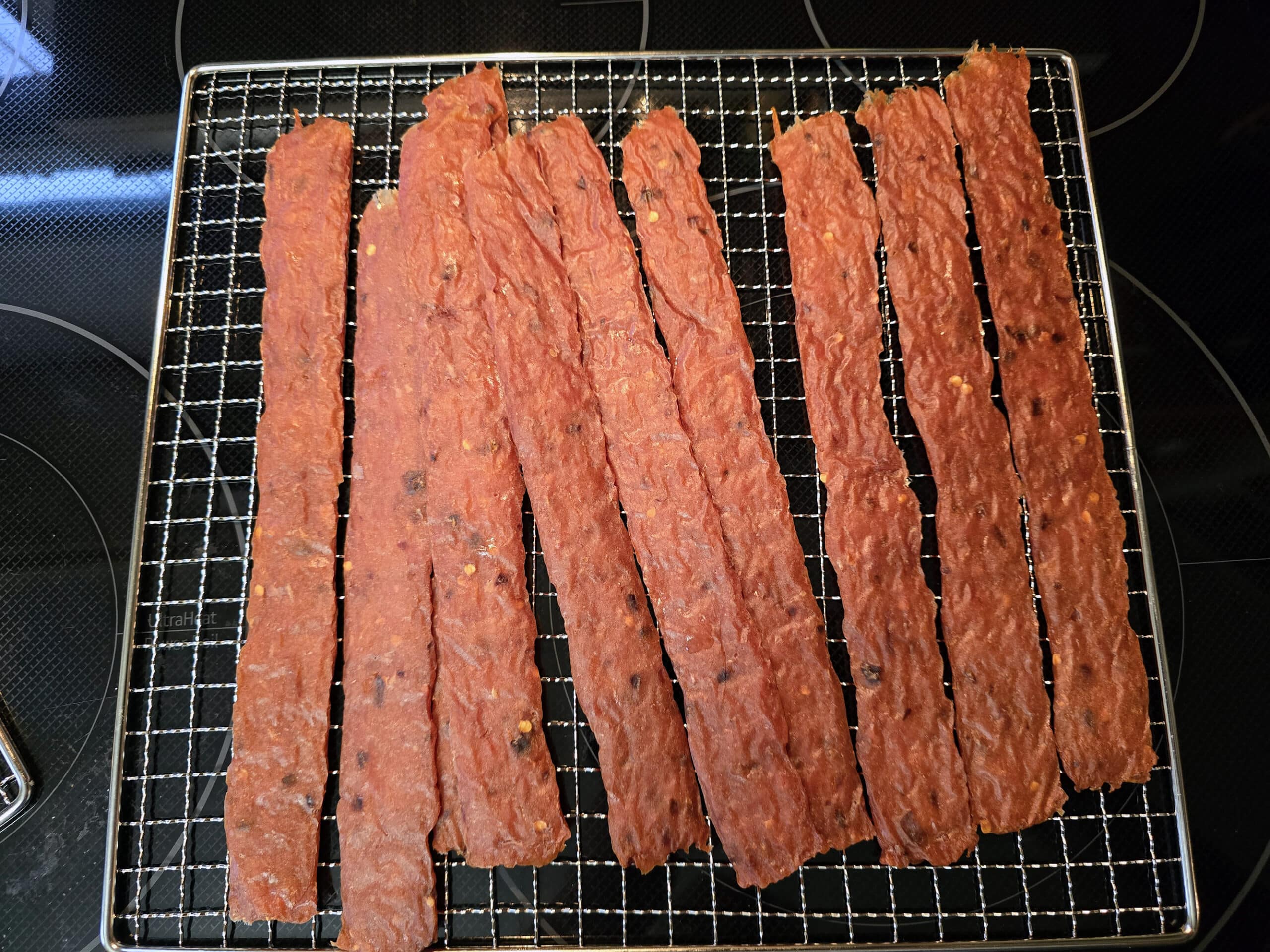 Several strips of spicy orange chicken jerky on a wire rack.