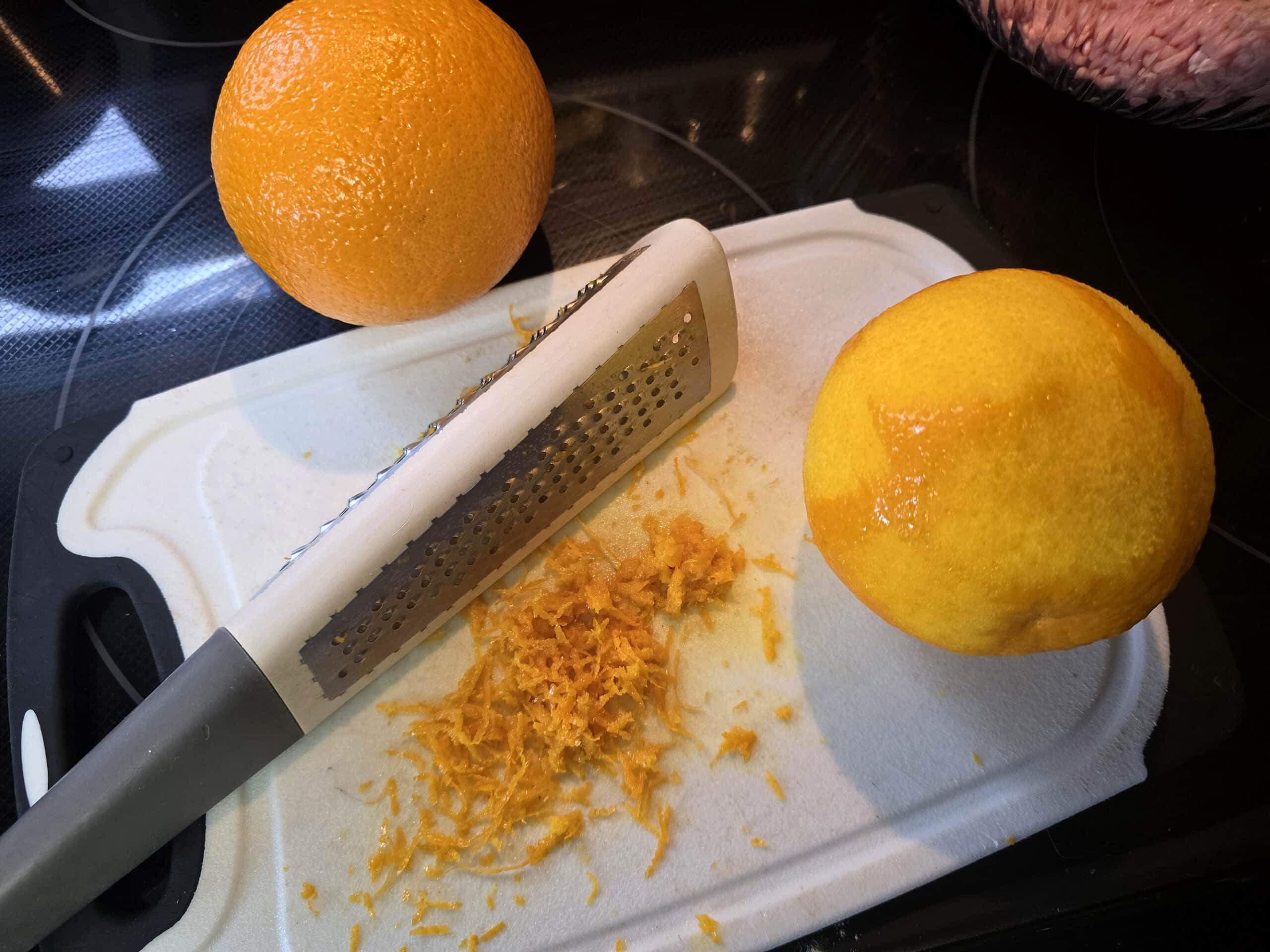 2 oranges being zested on a cutting board.