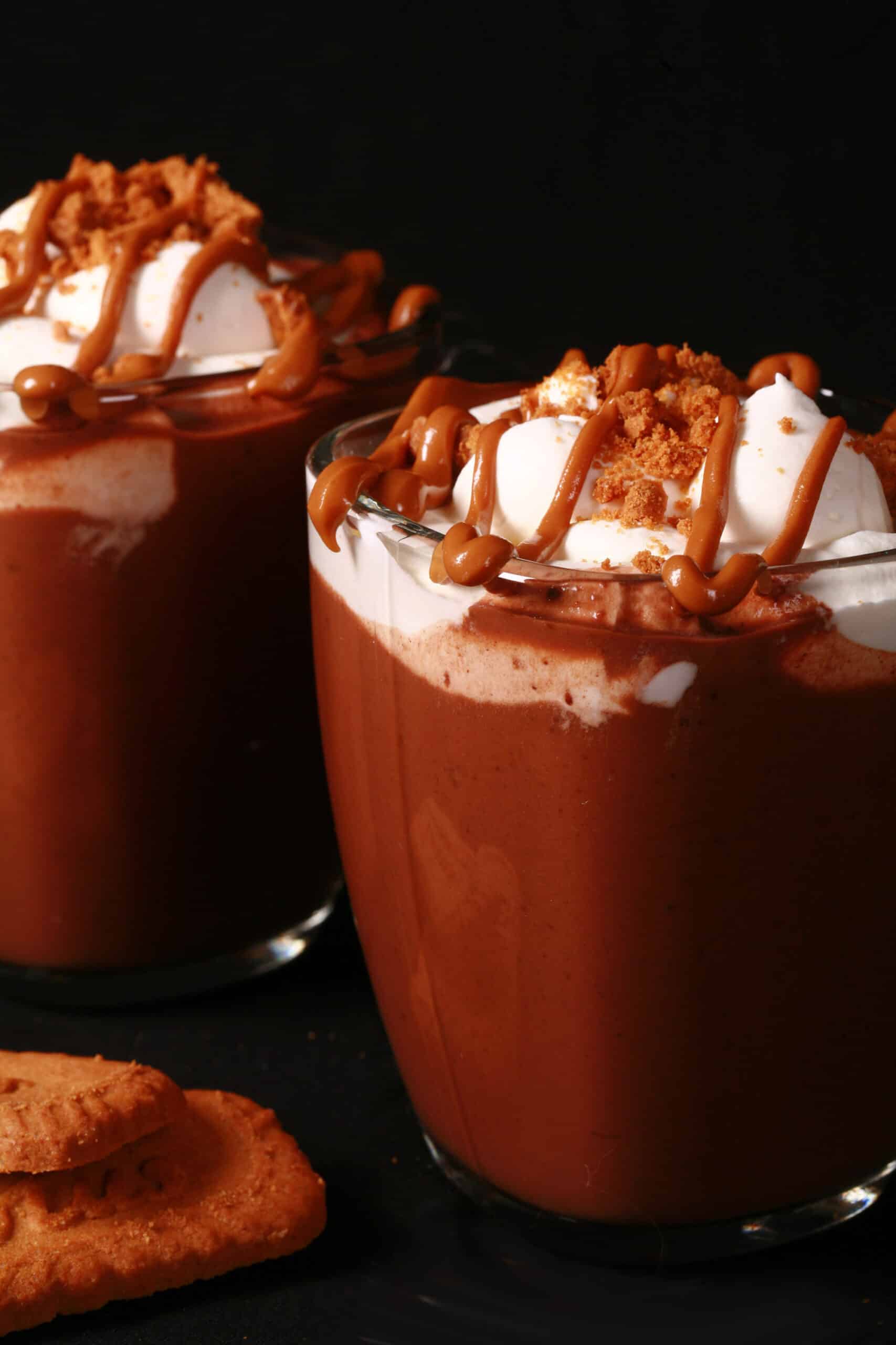 2 mugs of Biscoff hot cocoa, garnished with whipped cream, drizzled cookie butter, and crushed biscoff cookies.