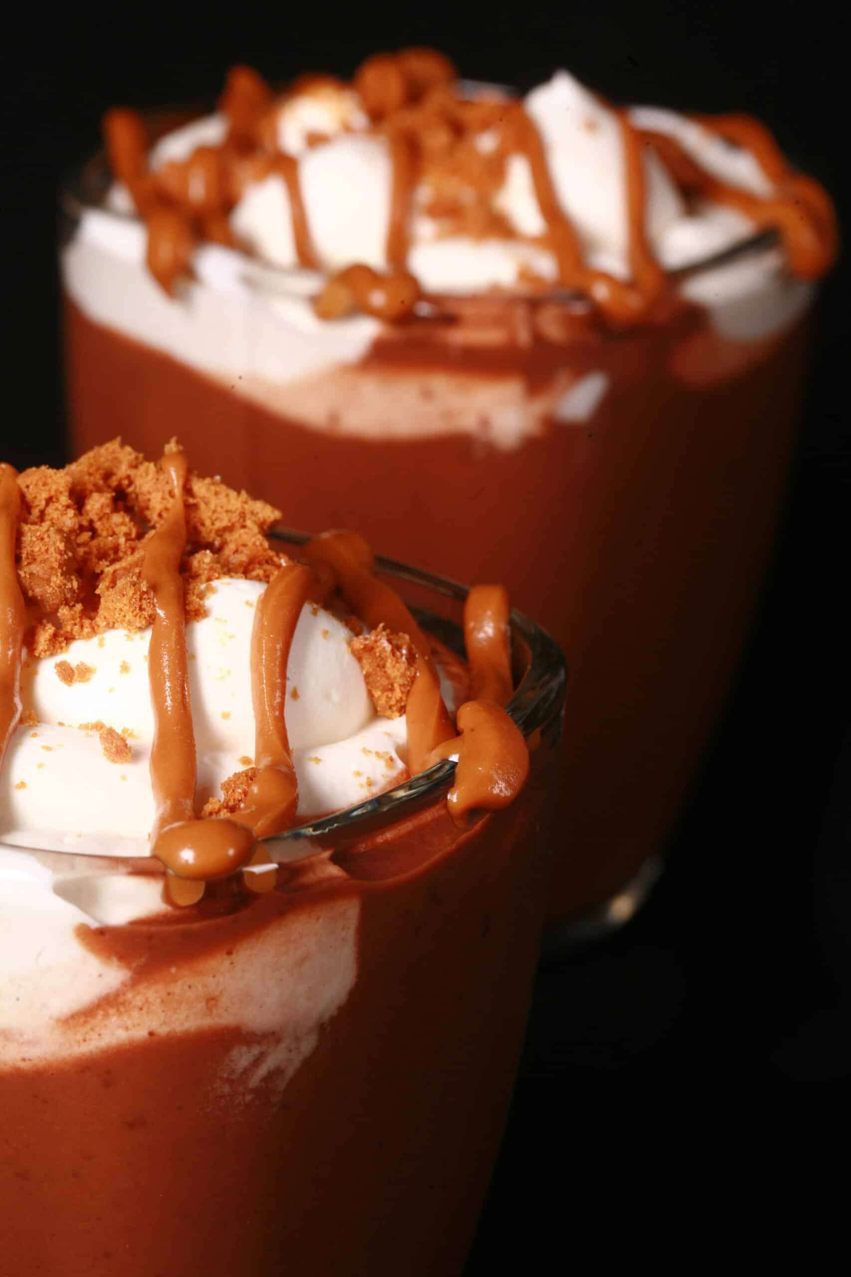 2 mugs of Biscoff hot chocolate, garnished with whipped cream, drizzled cookie butter, and crushed biscoff cookies.