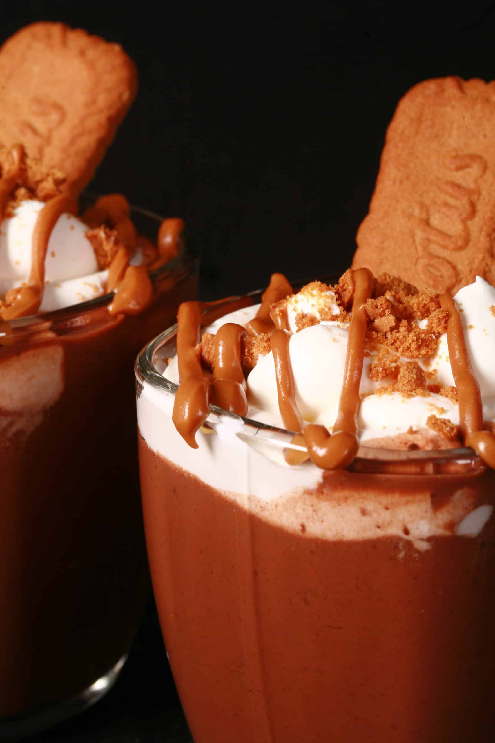 2 mugs of Biscoff hot cocoa, garnished with whipped cream, drizzled cookie butter, and crushed biscoff cookies.