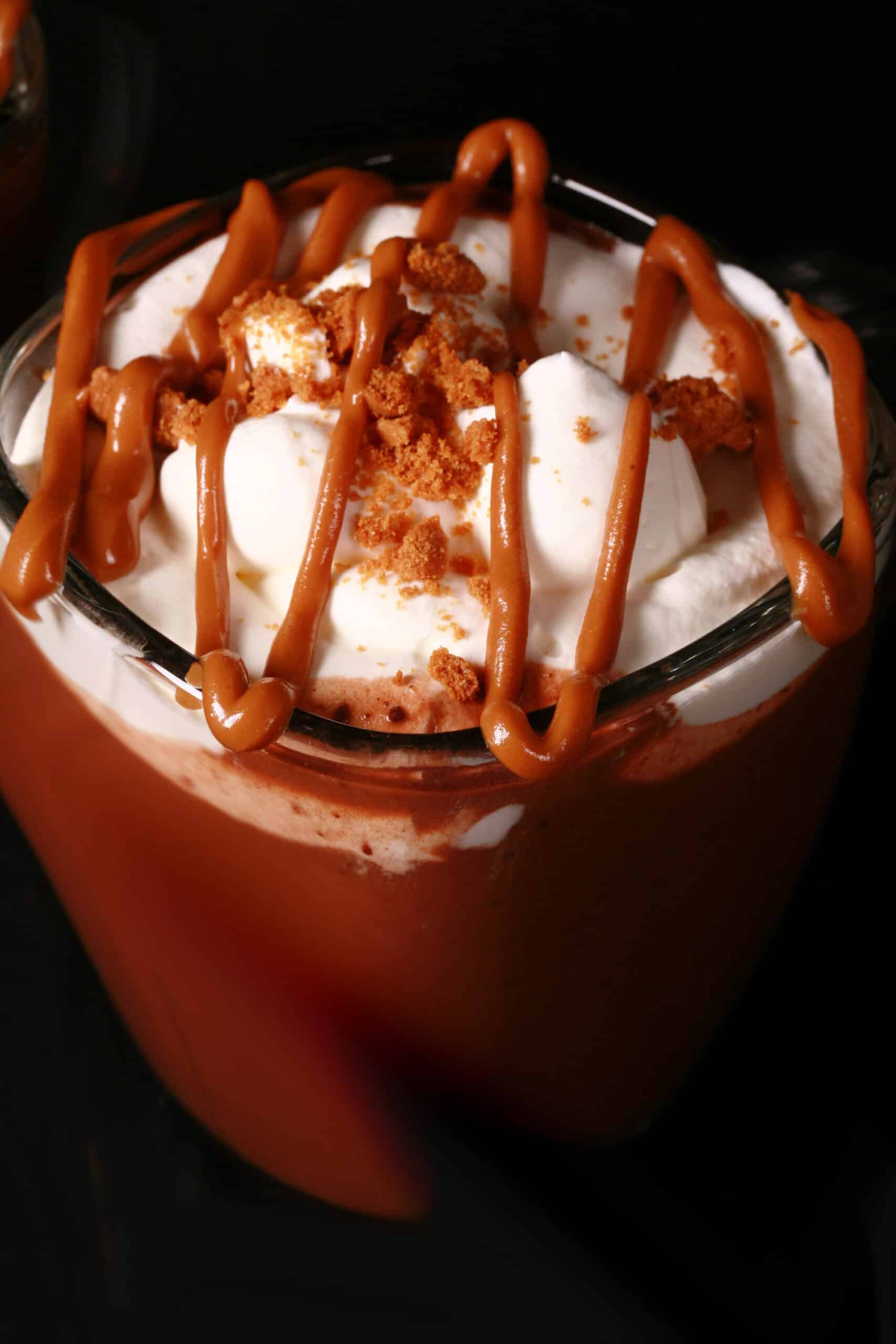 A mug of Biscoff hot chocolate, garnished with whipped cream, drizzled cookie butter, and crushed biscoff cookies.