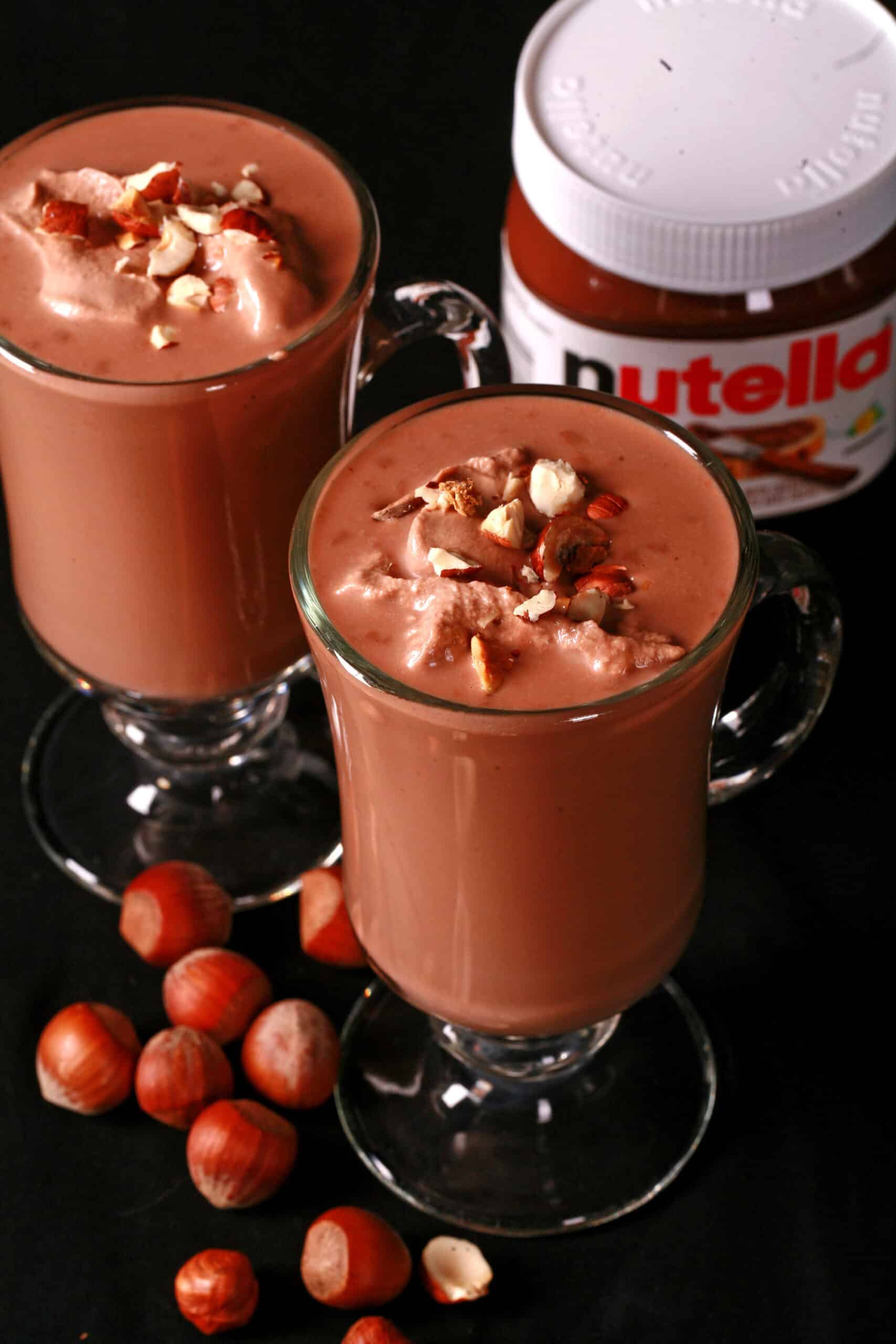 2 glass mugs of nutella hot chocolate, topped with nutella whipped cream and chopped hazelnuts.